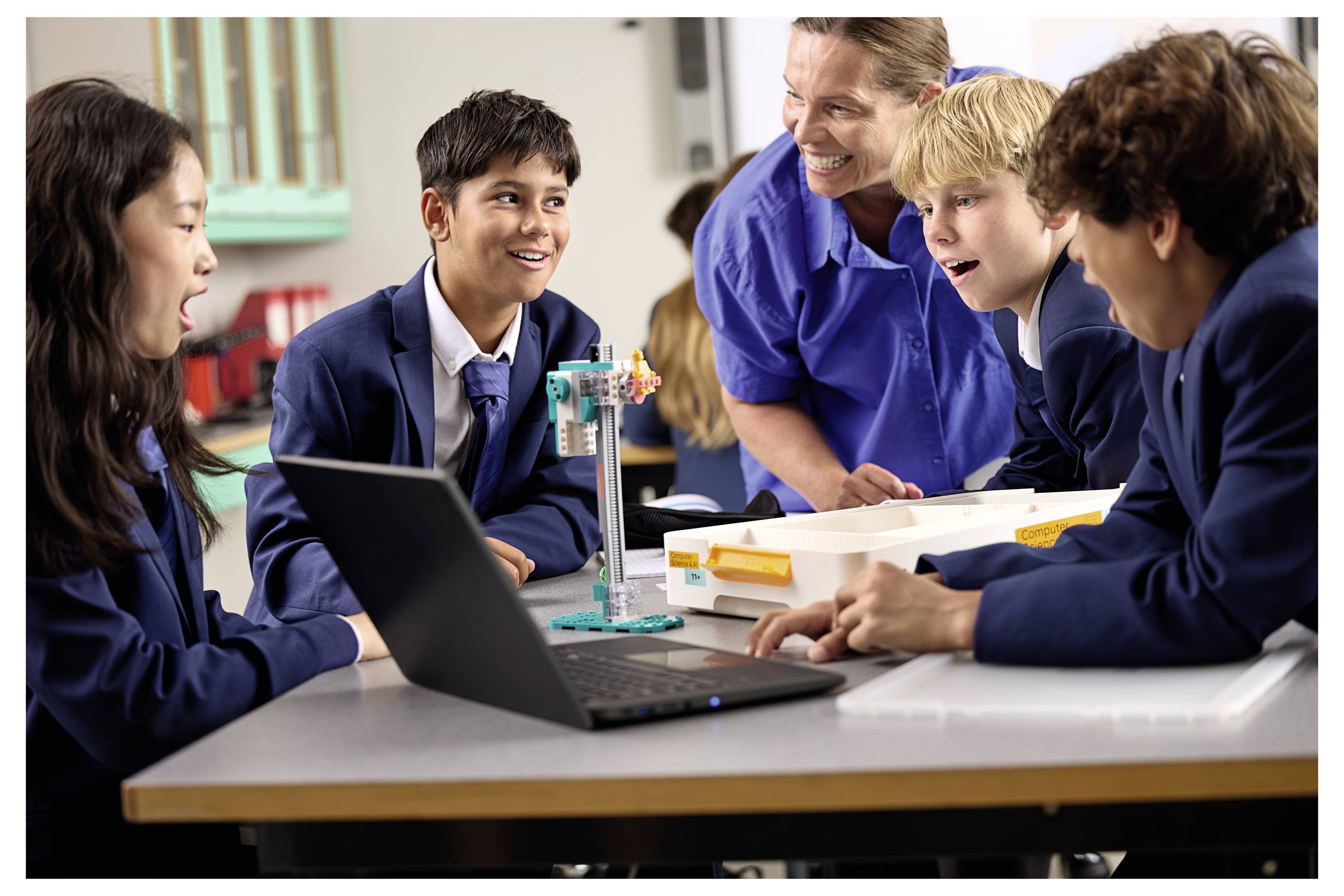 « Des étudiants et un enseignant engagés dans une expérience scientifique autour d'une table, entourés d'un ordinateur portable et de matériel pédagogique, dans une salle de classe. »