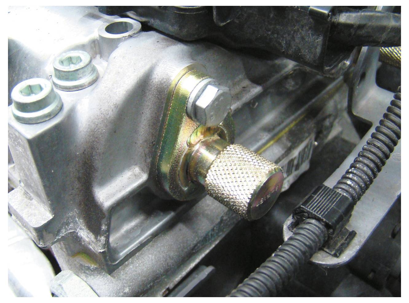Gros plan d'un ensemble de soupape métallique avec un bouton texturé et les pièces moteur environnantes, mettant en évidence son emplacement et ses connexions mécaniques.