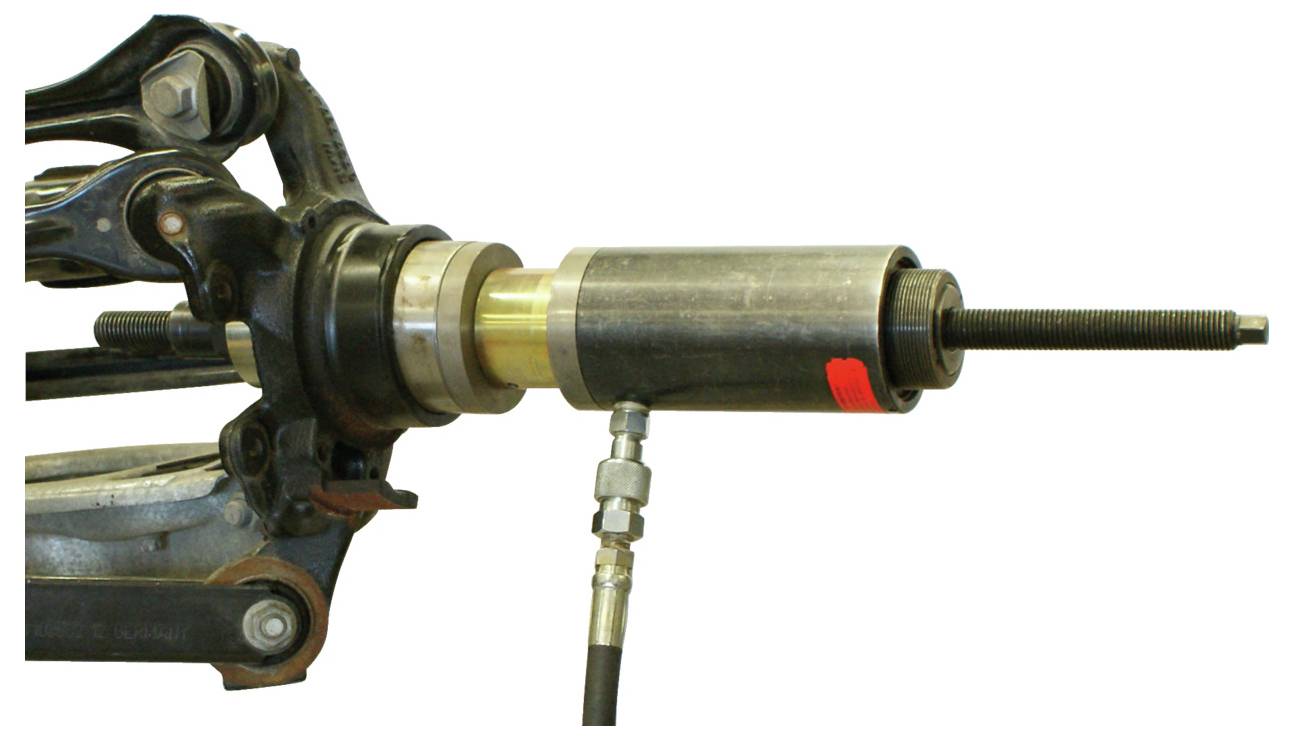 Un outil de cric hydraulique est montré en utilisation, appliquant une force aux composants mécaniques, probablement à des fins de maintenance ou de réparation.