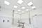 Une pièce avec un plafond haut dotée de luminaires LED carrés au plafond, deux tubes de ventilation, trois appareils muraux et une table marron.