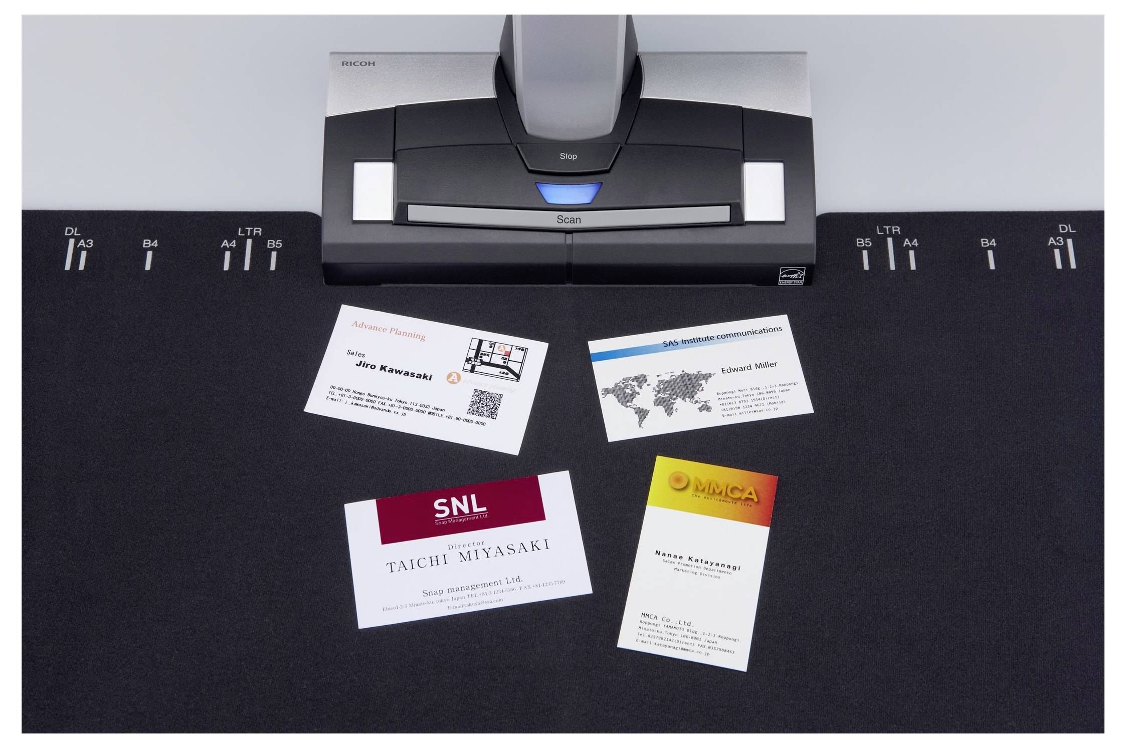 Un scanner avec quatre cartes de visite sur une surface de tapis noir, chaque carte présentant des designs différents et des informations de contact.