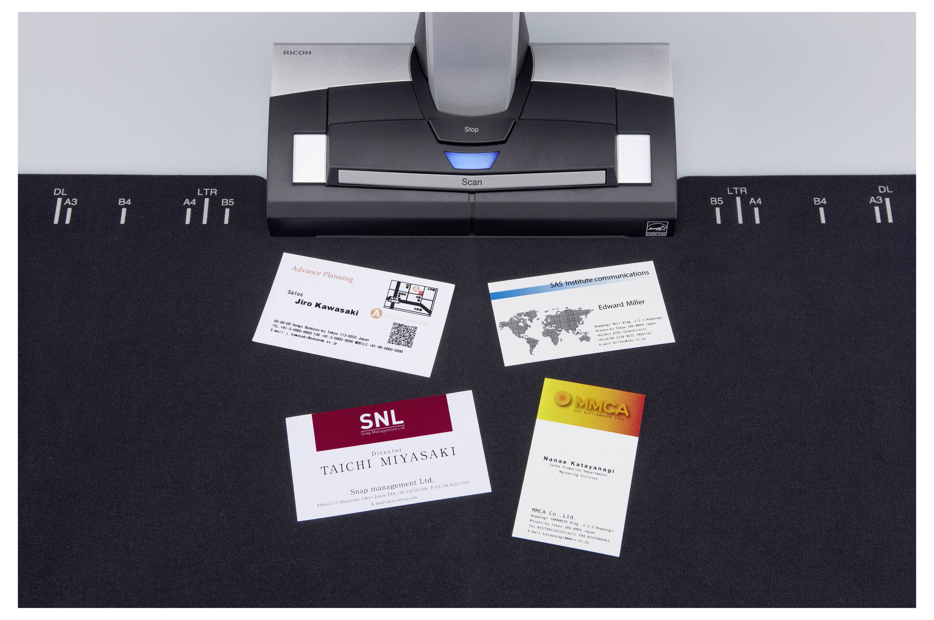 Un scanner de cartes de visite avec quatre cartes sur un tapis noir. Les cartes affichent différents noms, logos et codes QR, suggérant des identités commerciales diverses.