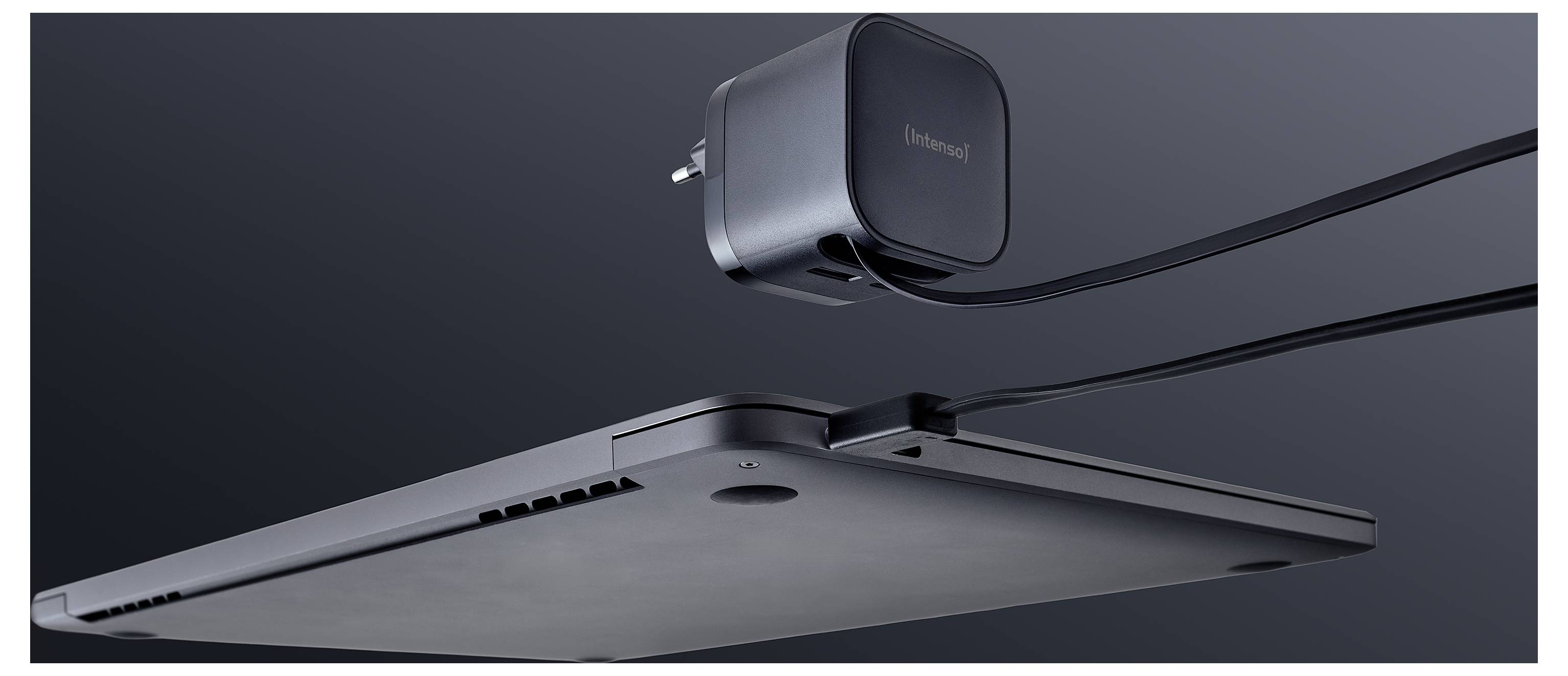 Un fin ordinateur portable vu de côté, affichant un profil élancé, connecté à un adaptateur d'alimentation avec un câble, sur un fond sombre.
