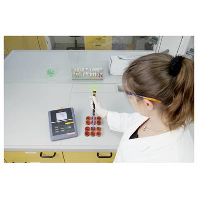Un scientifique en blouse de laboratoire utilisant une pipette sur des boîtes de Pétri placées sur une table de laboratoire. Une balance numérique et des échantillons colorés sont visibles à proximité.