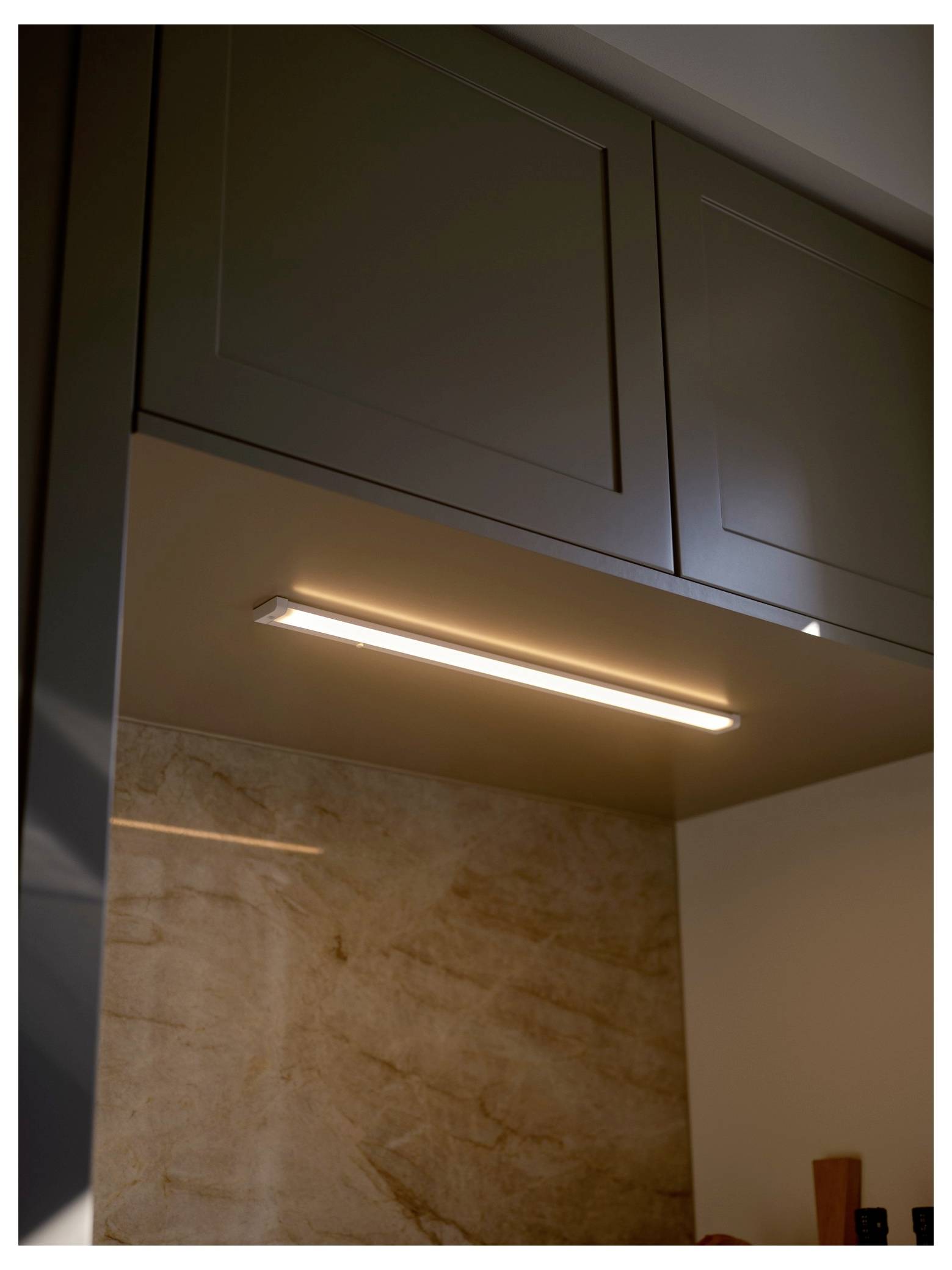 L'éclairage sous les armoires illumine le dosseret en pierre beige dans une cuisine, mettant en évidence la texture lisse et ajoutant une lumière d'ambiance.
