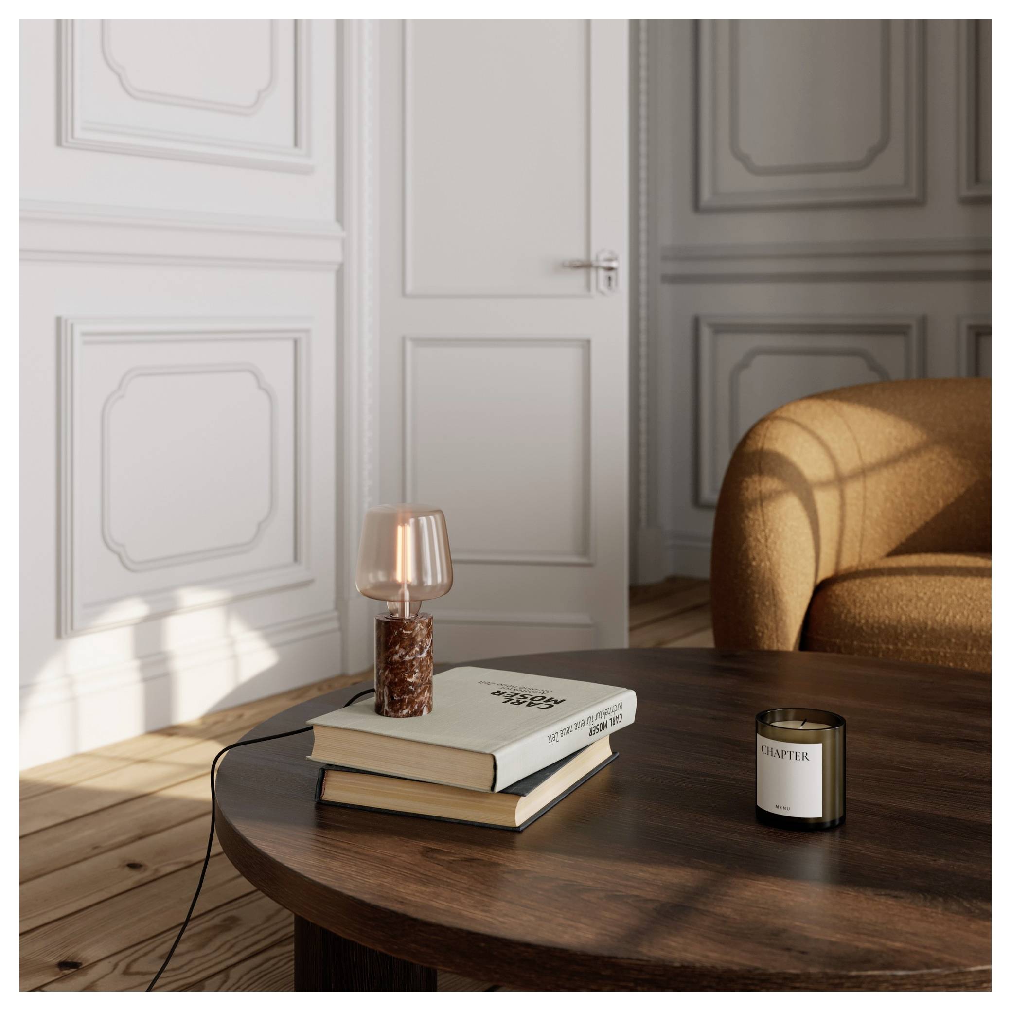 Une pièce confortable avec une table en bois, deux livres empilés, une petite lampe et une bougie. La lumière du soleil projette des ombres sur le sol en bois dur et les murs.