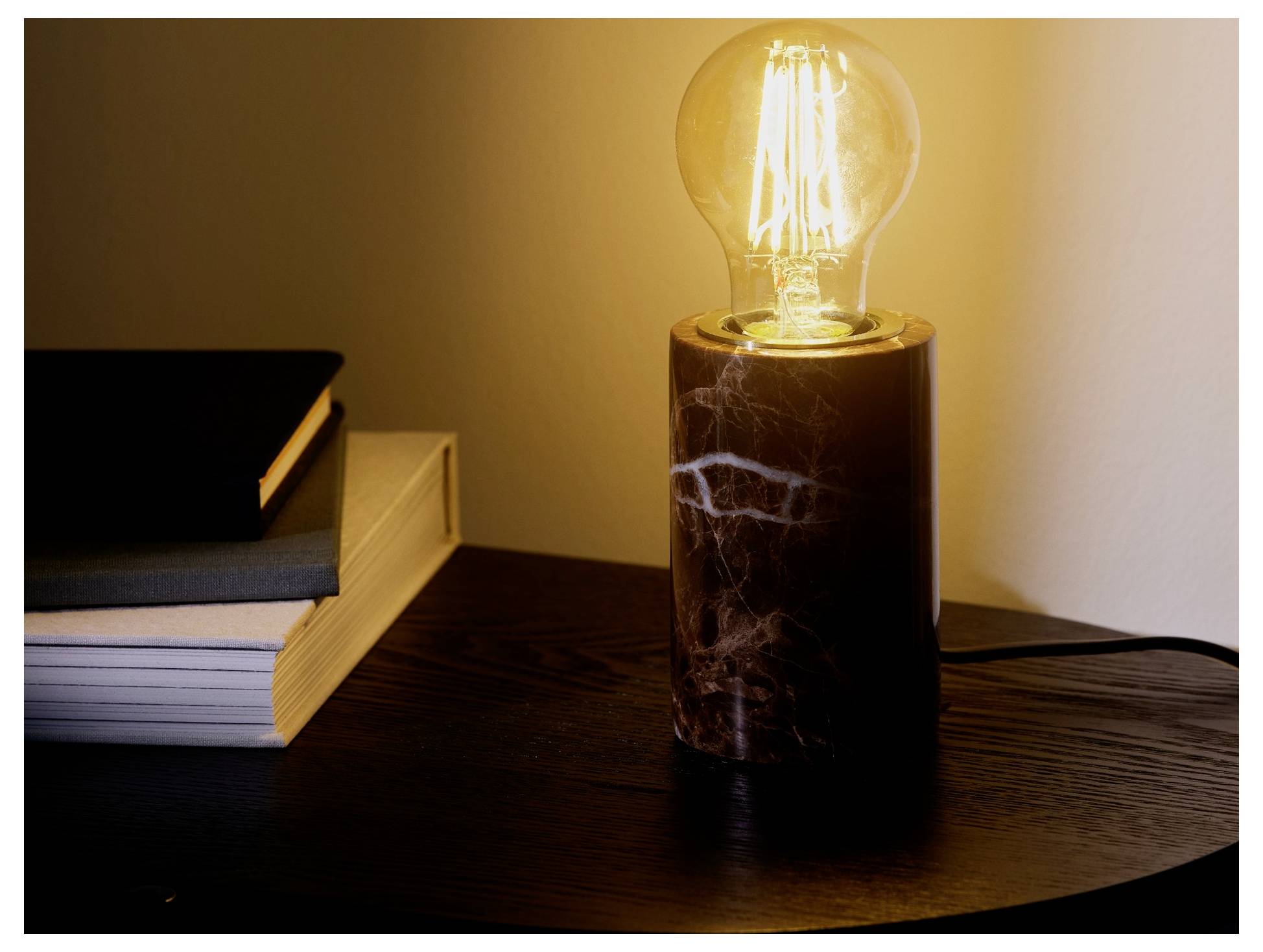 Une ampoule électrique brillante sur une table en bois sombre à côté d'une pile de livres, créant une atmosphère chaleureuse et confortable.