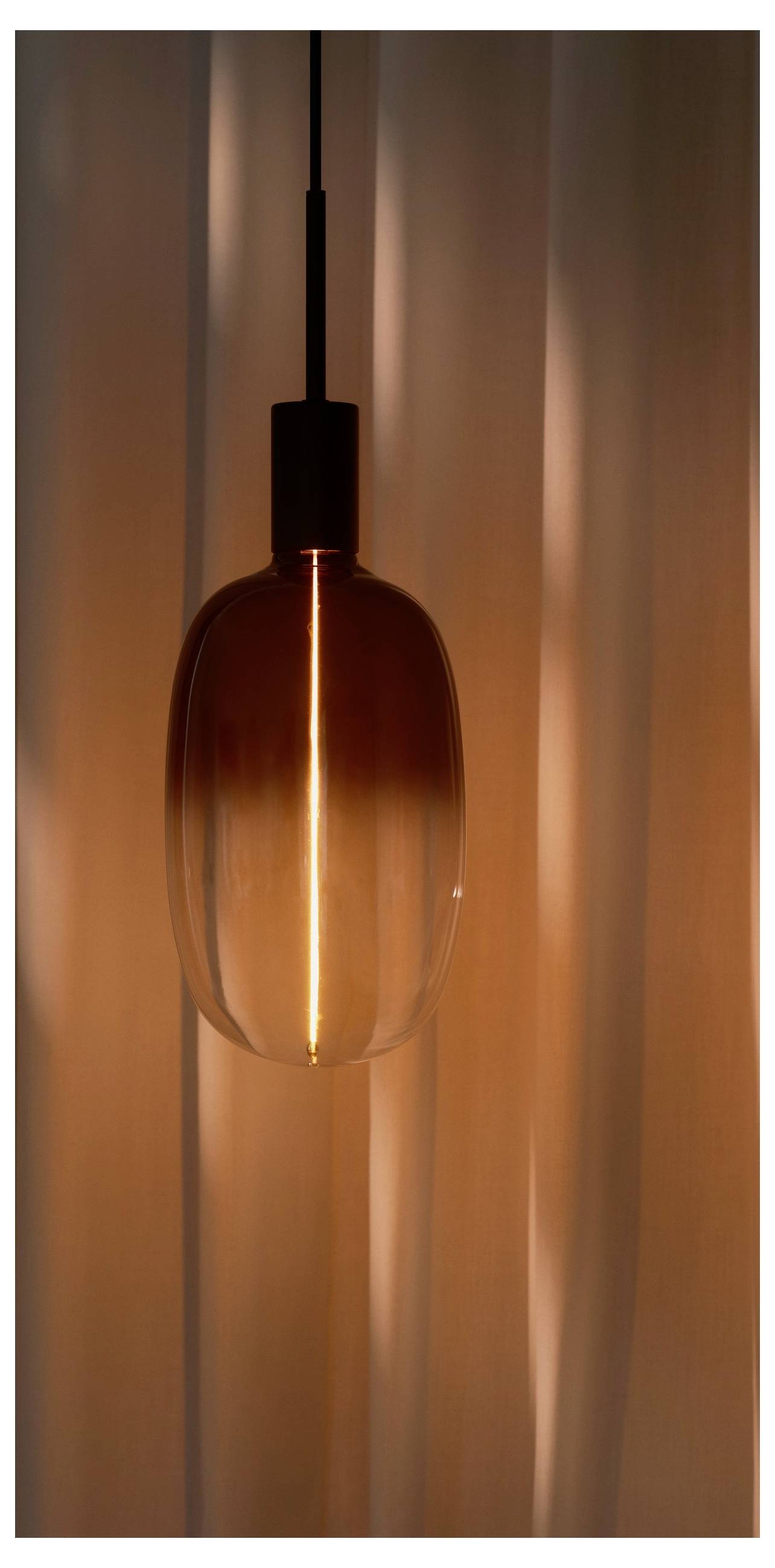 Une lampe suspendue en verre ambré crée une lumière chaleureuse sur un arrière-plan aux textures douces, créant une atmosphère confortable et accueillante.