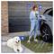 Une personne vêtue de vêtements bleus recharge une voiture électrique tout en tenant un téléphone. À proximité, un chien blanc pelucheux est allongé sur le sol.