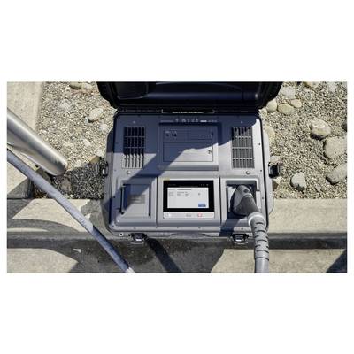 Une station de recharge ouverte avec un écran numérique affichant un message de statut à côté d'un câble de recharge branché, posé sur un sol pavé de galets.