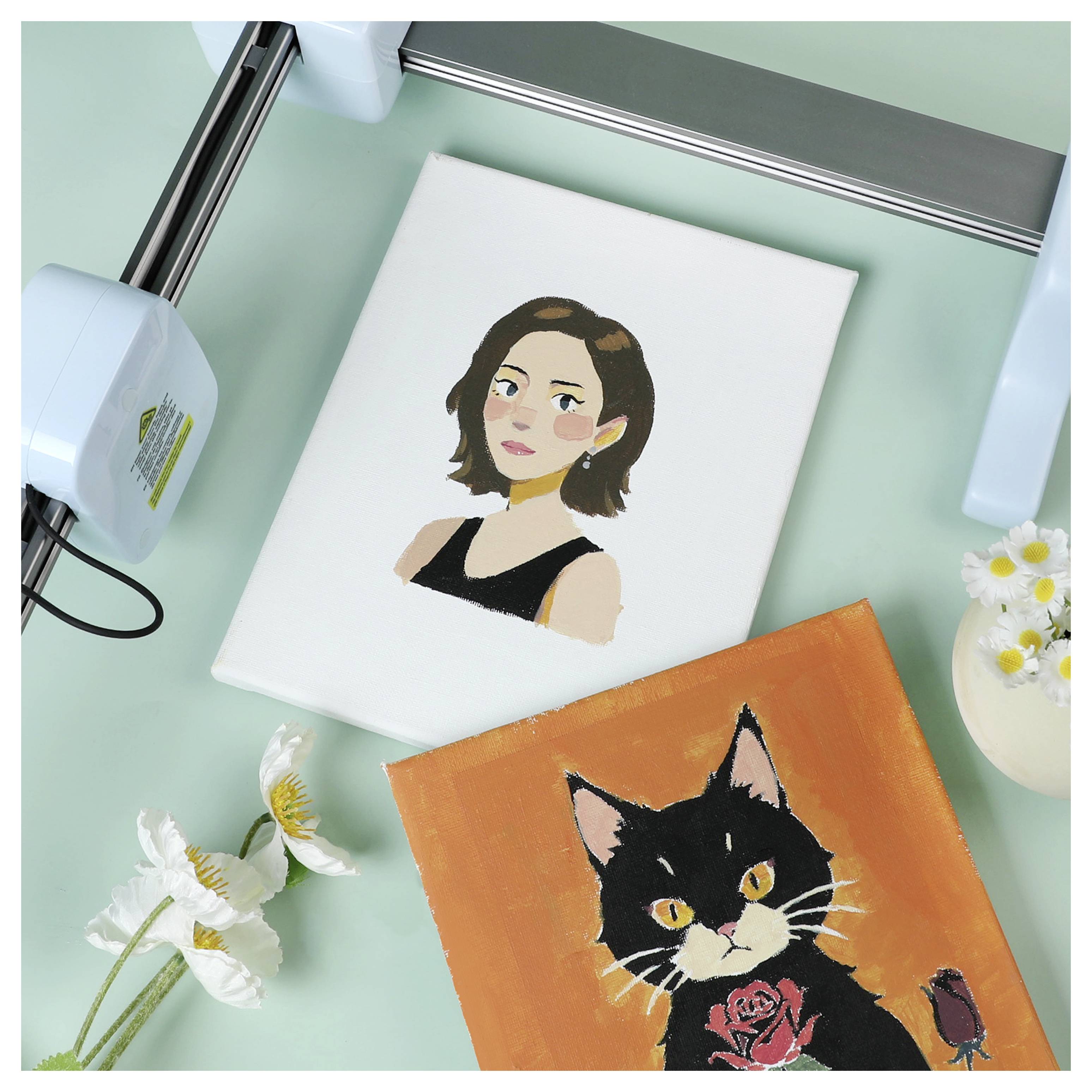 Une toile avec une peinture d'une femme aux cheveux noirs courts vêtue d'un haut noir ; une autre toile représente un chat noir avec une rose sur fond orange.