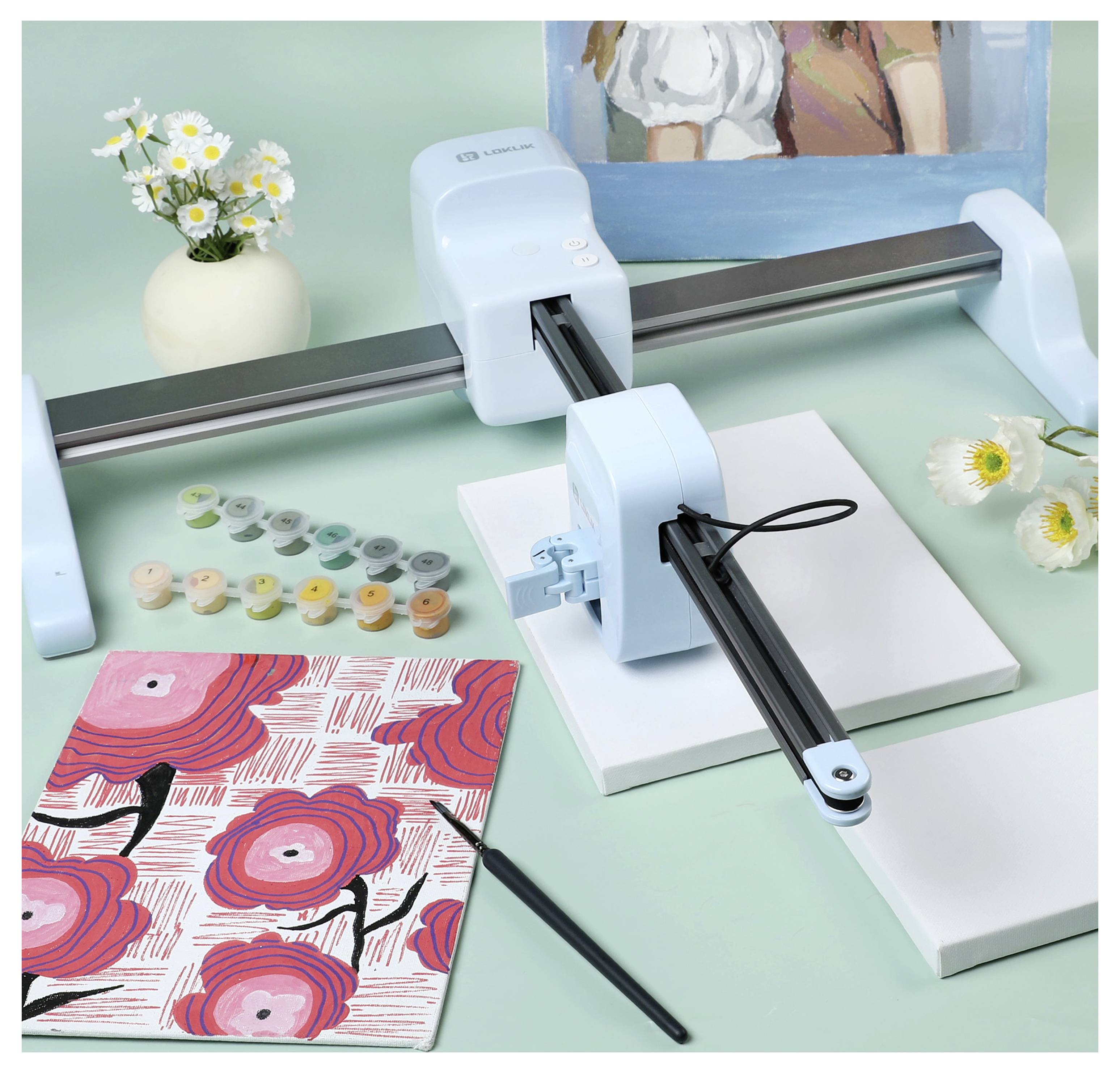 Un robot artistique est prêt à peindre sur une toile vierge, entouré de pots de peinture, d'un carnet à motifs, d'un pinceau et de fleurs.