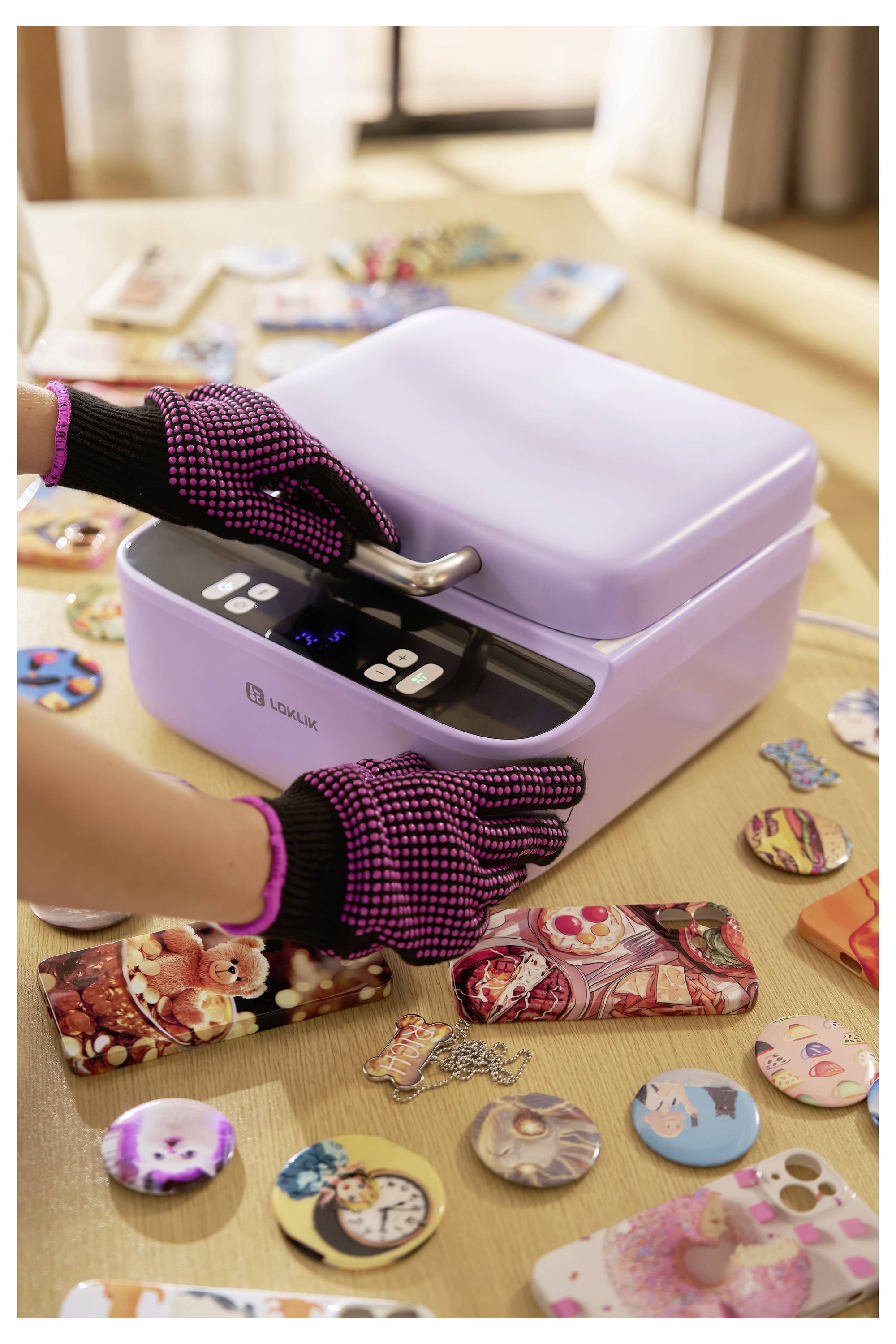 Une personne portant des gants utilise une machine de sublimation sur une table remplie de coques de téléphone colorées et de badges.