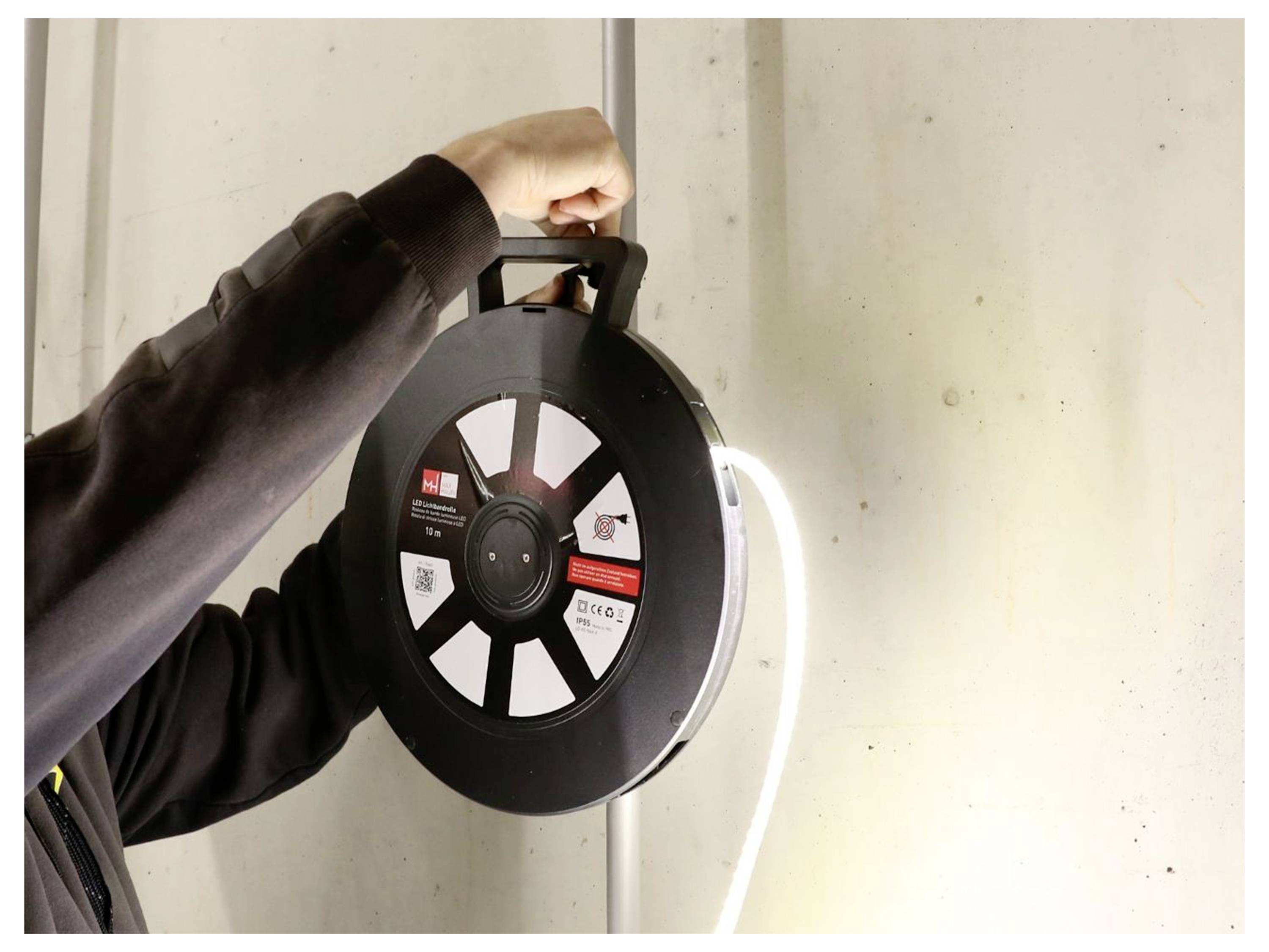 Une personne tenant une grande bobine de câble blanc, montée sur un mur, vraisemblablement pour une installation électrique ou de données.