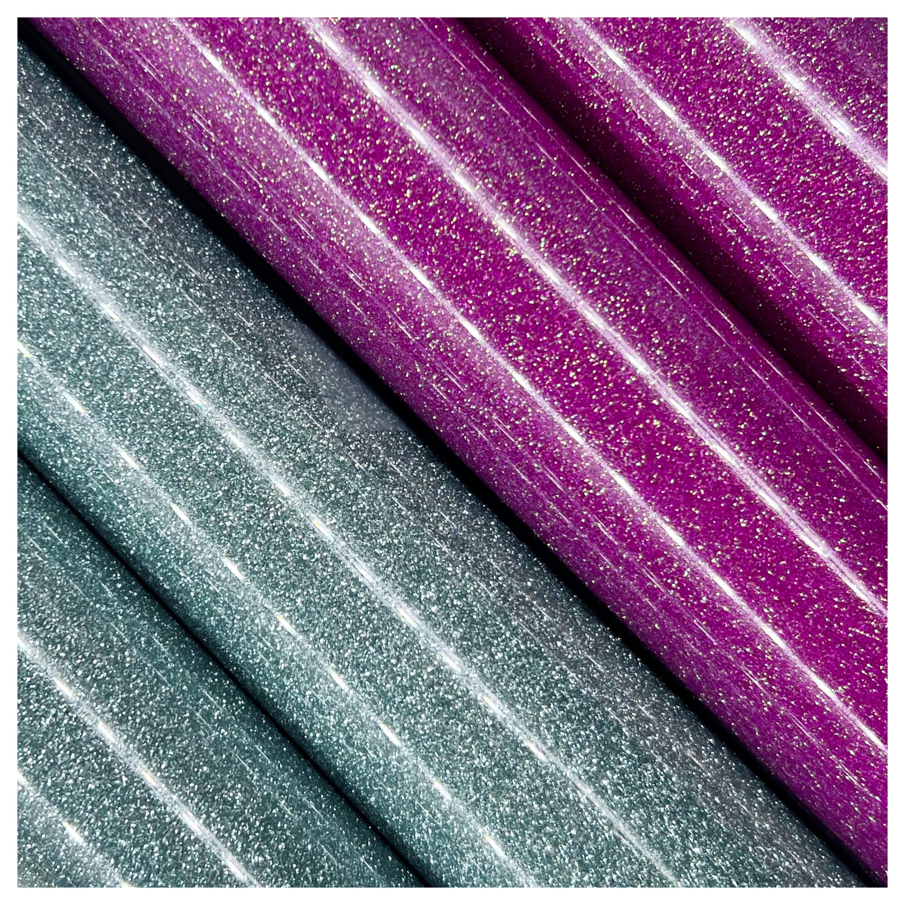 Gros plan de rouleaux de papier à paillettes scintillantes, avec trois rouleaux bleu-vert et deux rouleaux magenta, mettant en avant la texture chatoyante et le contraste des couleurs.