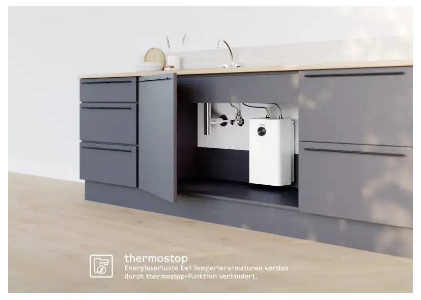 Une cuisine moderne avec des armoires grises. Une porte d'armoire est ouverte, révélant la plomberie et un chauffe-eau compact sous l'évier.
