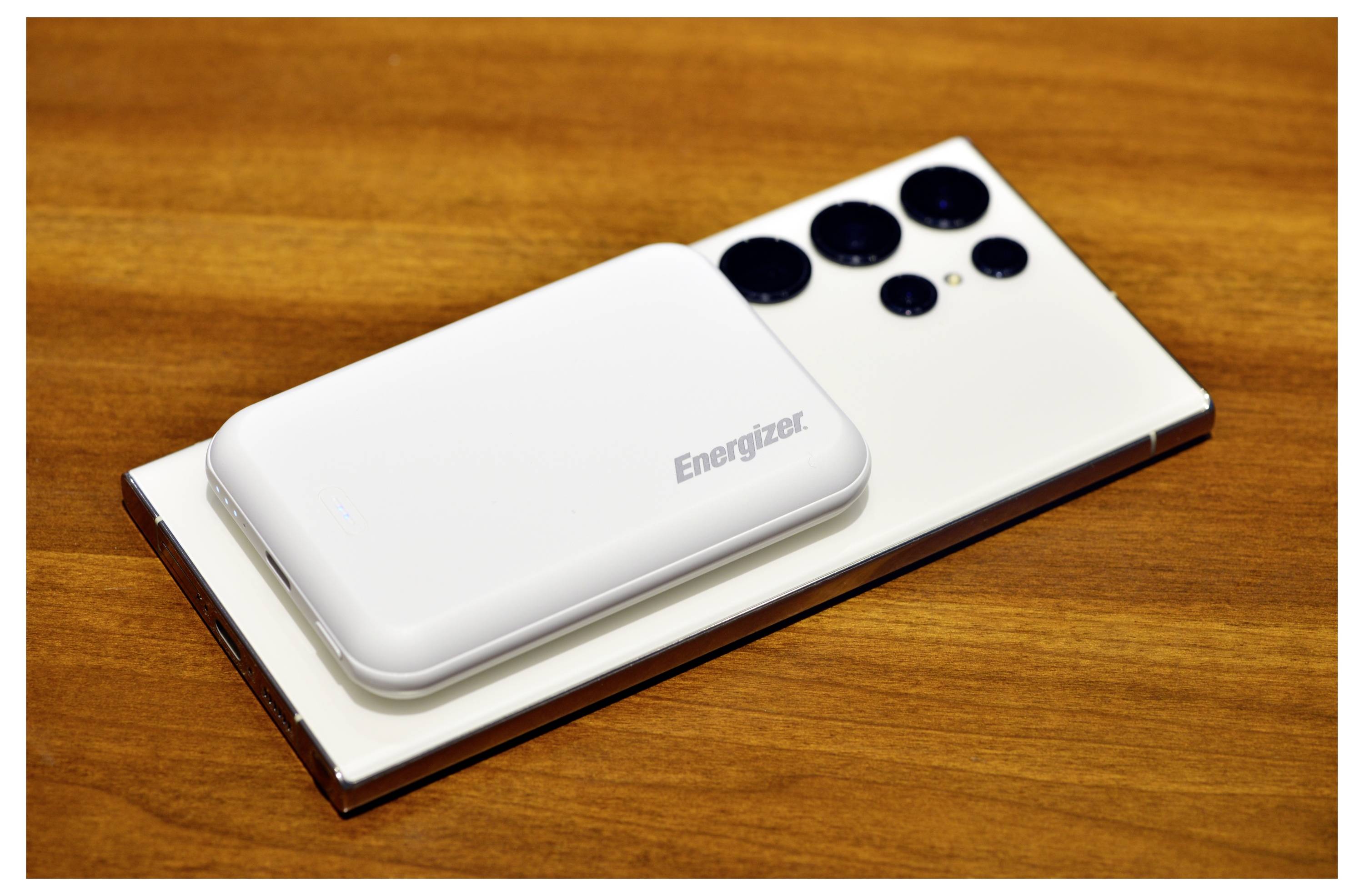 Un chargeur portable Energizer blanc est placé sur un smartphone blanc avec plusieurs objectifs, sur une surface en bois.
