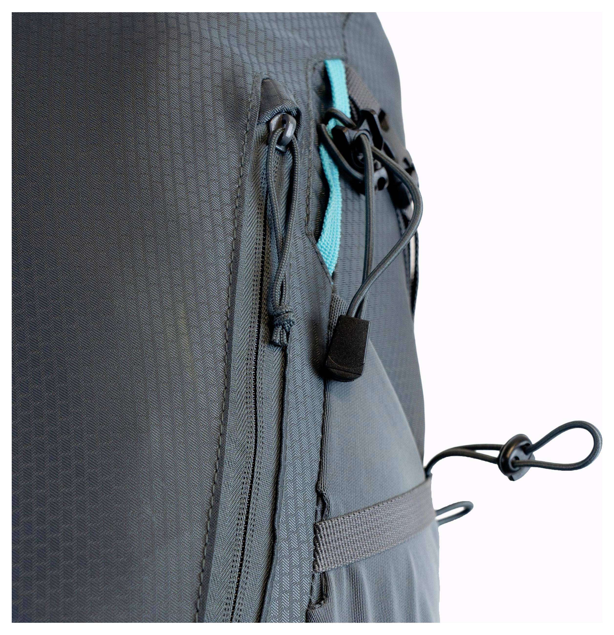 Gros plan d'un sac à dos en tissu foncé texturé, montrant un accent bleu-vert, une poche zippée et une corde sur le côté pour l'ajustement.