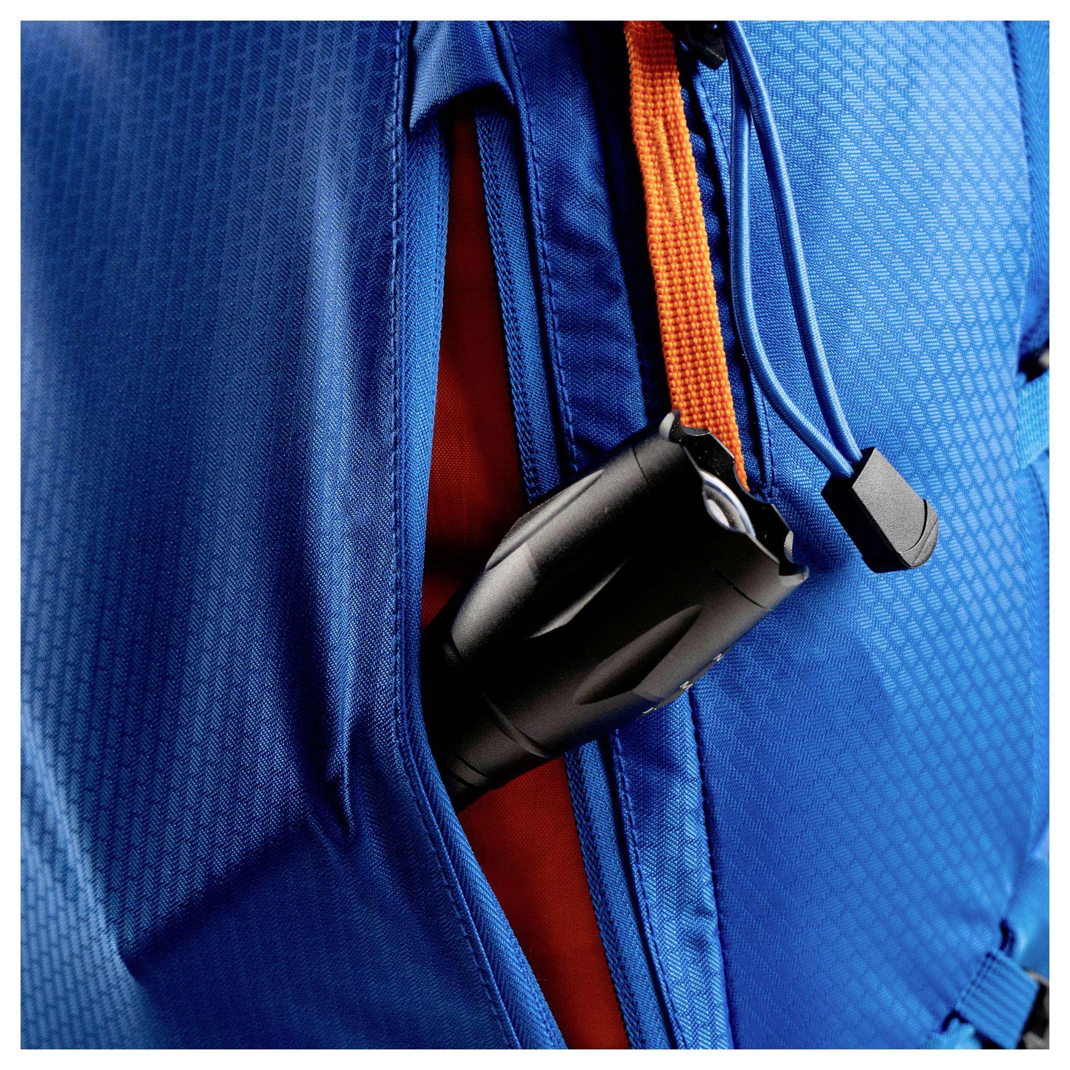 Une lampe de poche noire est accrochée à une sangle orange à l'intérieur de la poche d'un sac à dos bleu.