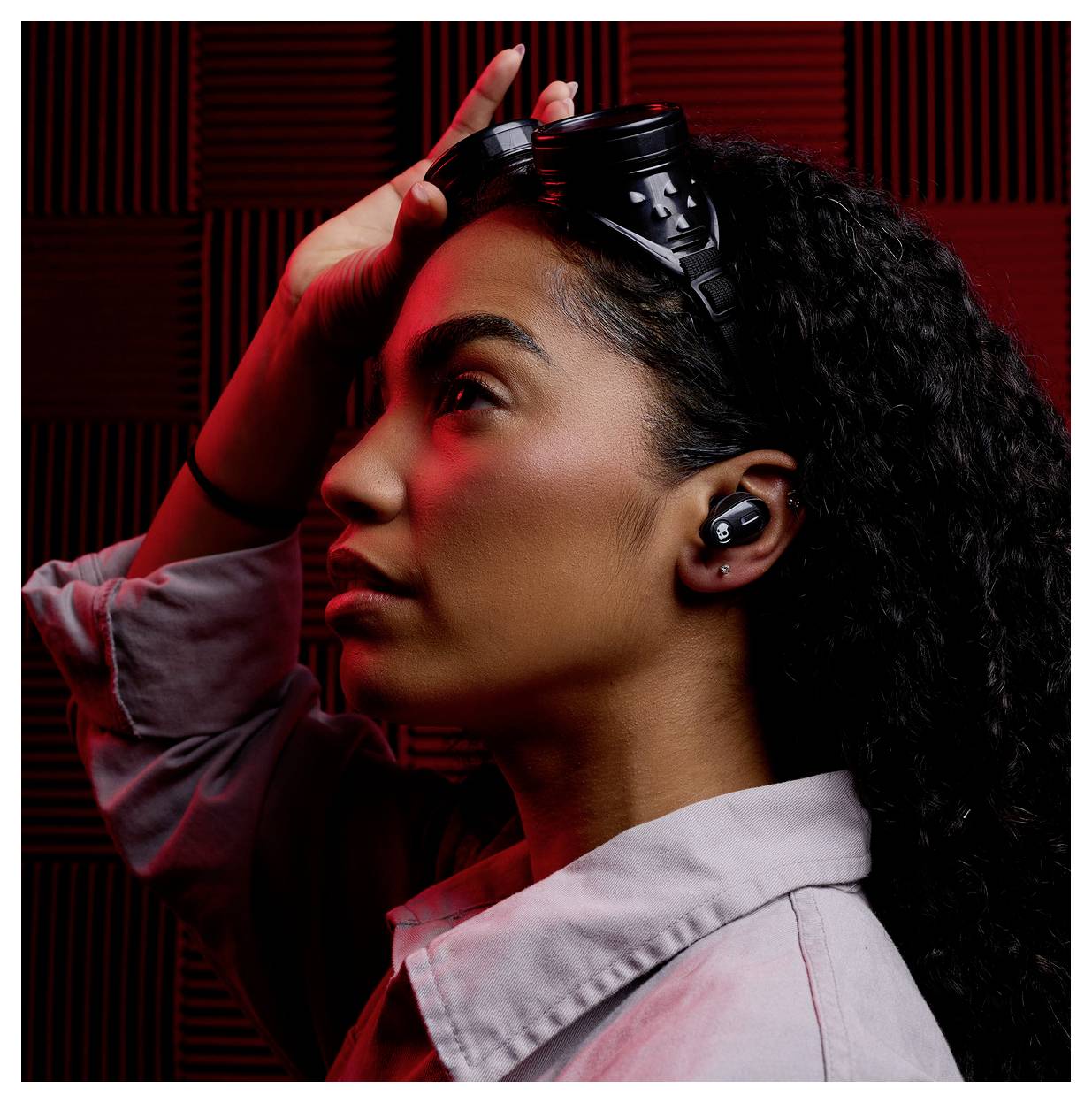 Une personne de profil portant des écouteurs sans fil et se touchant la tête. Un éclairage rouge crée un effet dramatique sur le visage.