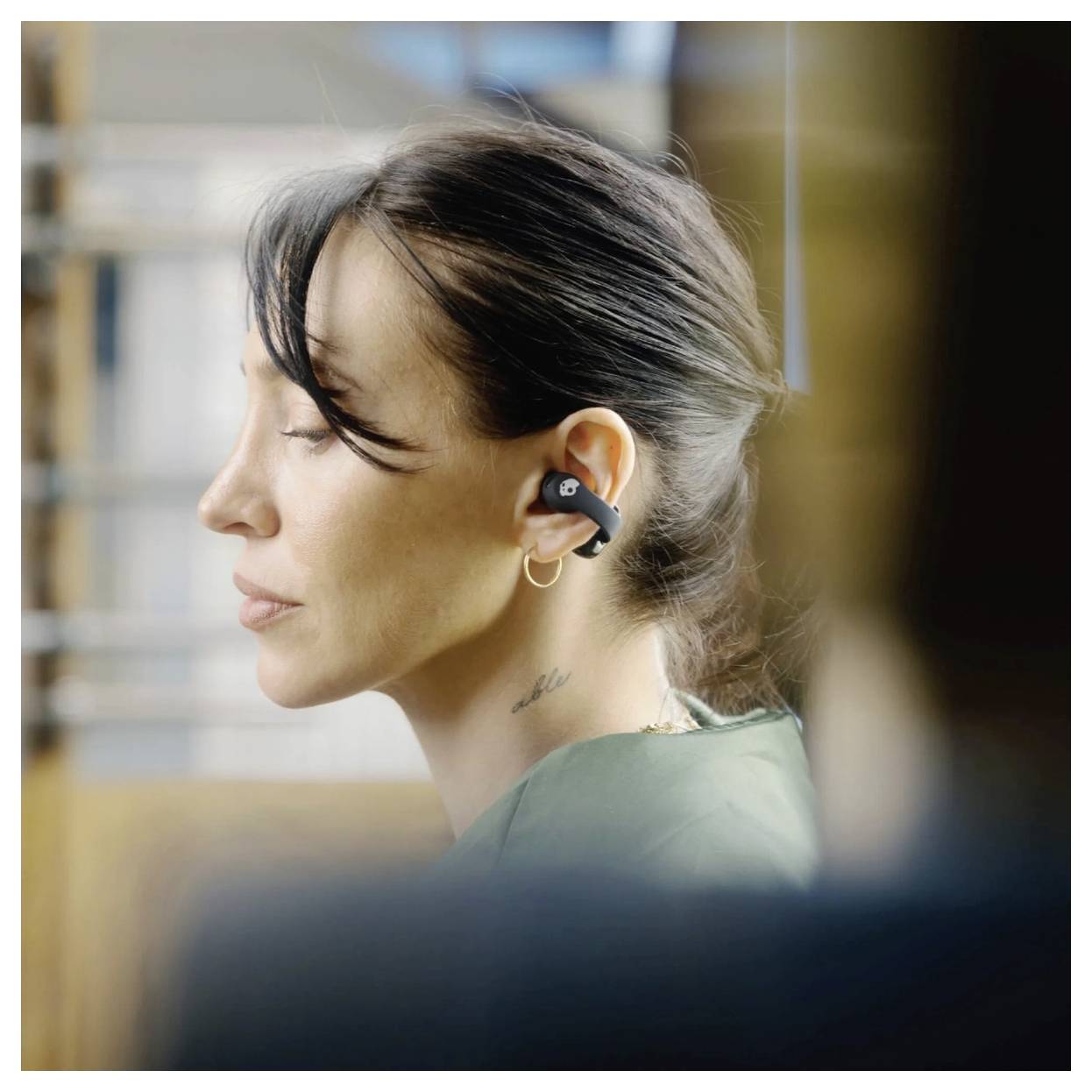 Une femme les yeux fermés porte des écouteurs sans fil dans un cadre intérieur, dégageant une sensation de détente et de concentration.