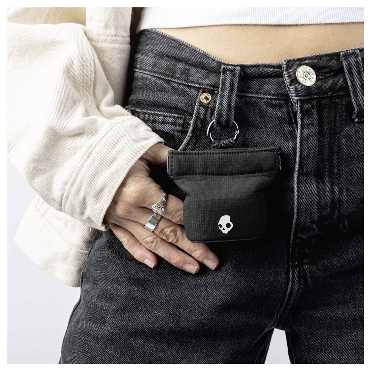 Une personne portant un jean noir avec une petite pochette noire attachée à la taille. La pochette est ornée d'une petite icône de crâne blanc.