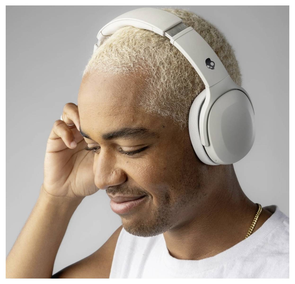 Une personne aux cheveux blonds courts sourit et écoute de la musique avec de grands écouteurs supra-auriculaires blancs.