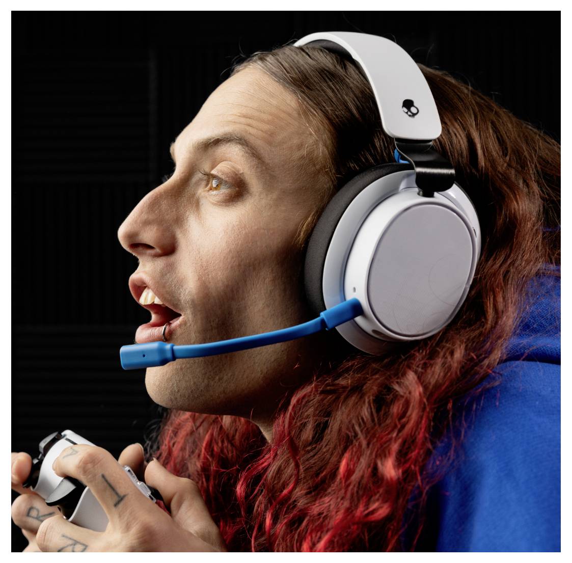 Une personne aux cheveux longs portant un casque est intensément concentrée, probablement en train de jouer, tenant une manette de console, sur un fond sombre.