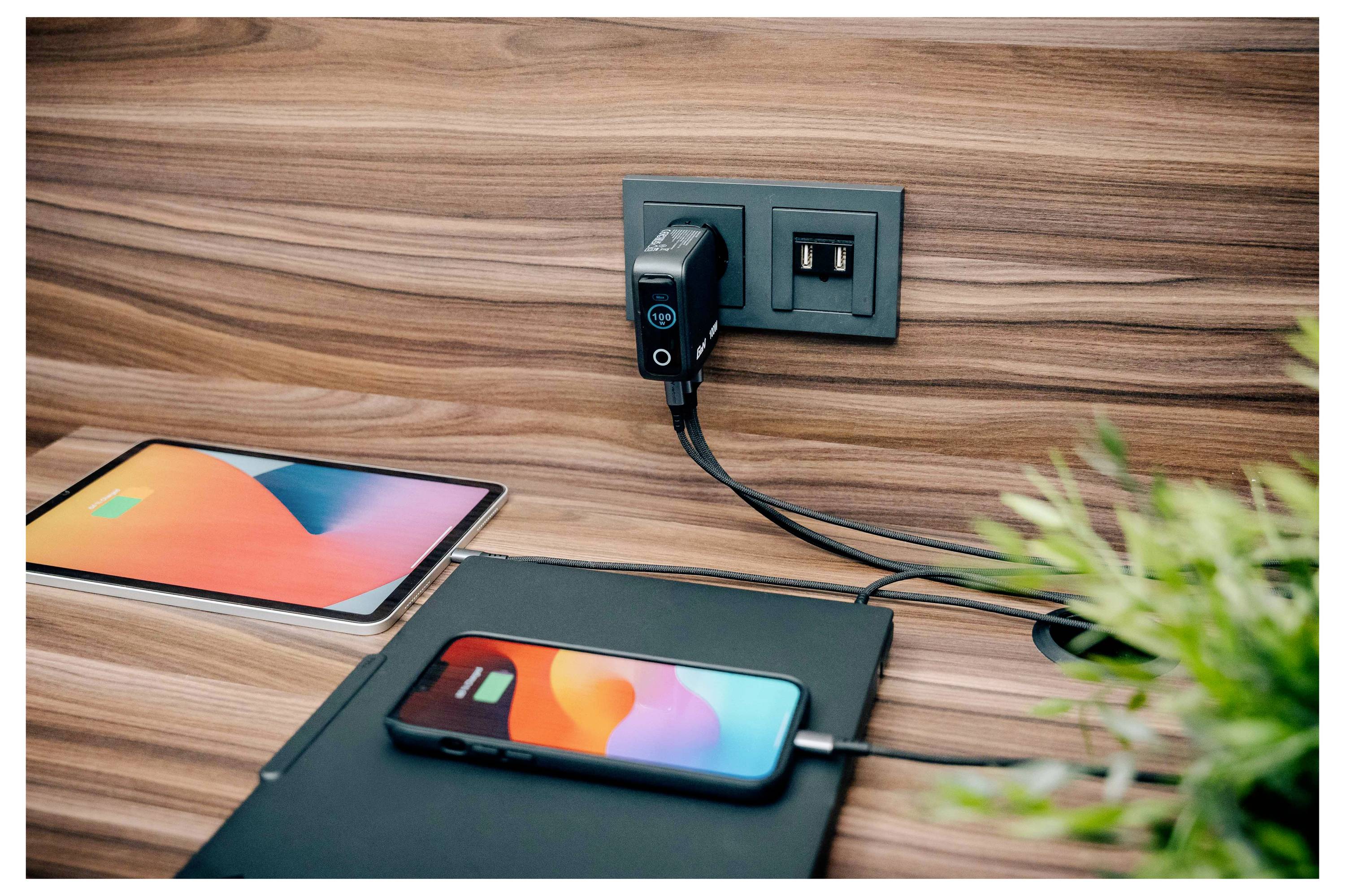 Un téléphone intelligent et une tablette en charge sur un bureau en bois, tous deux connectés à une prise murale avec ports USB.