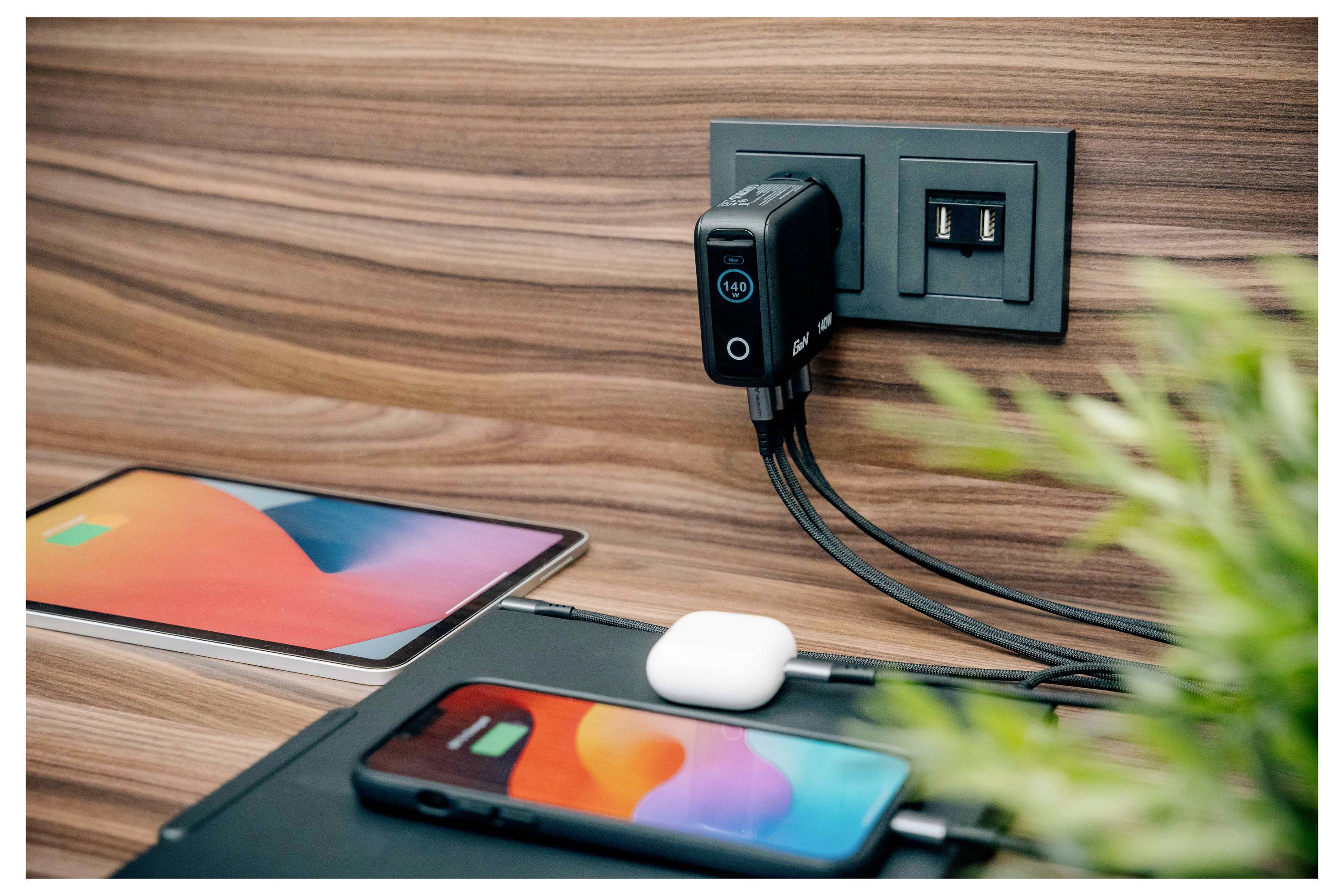 Un téléphone et une tablette se chargent via un adaptateur de prise murale ; une paire d'écouteurs repose sur la table.