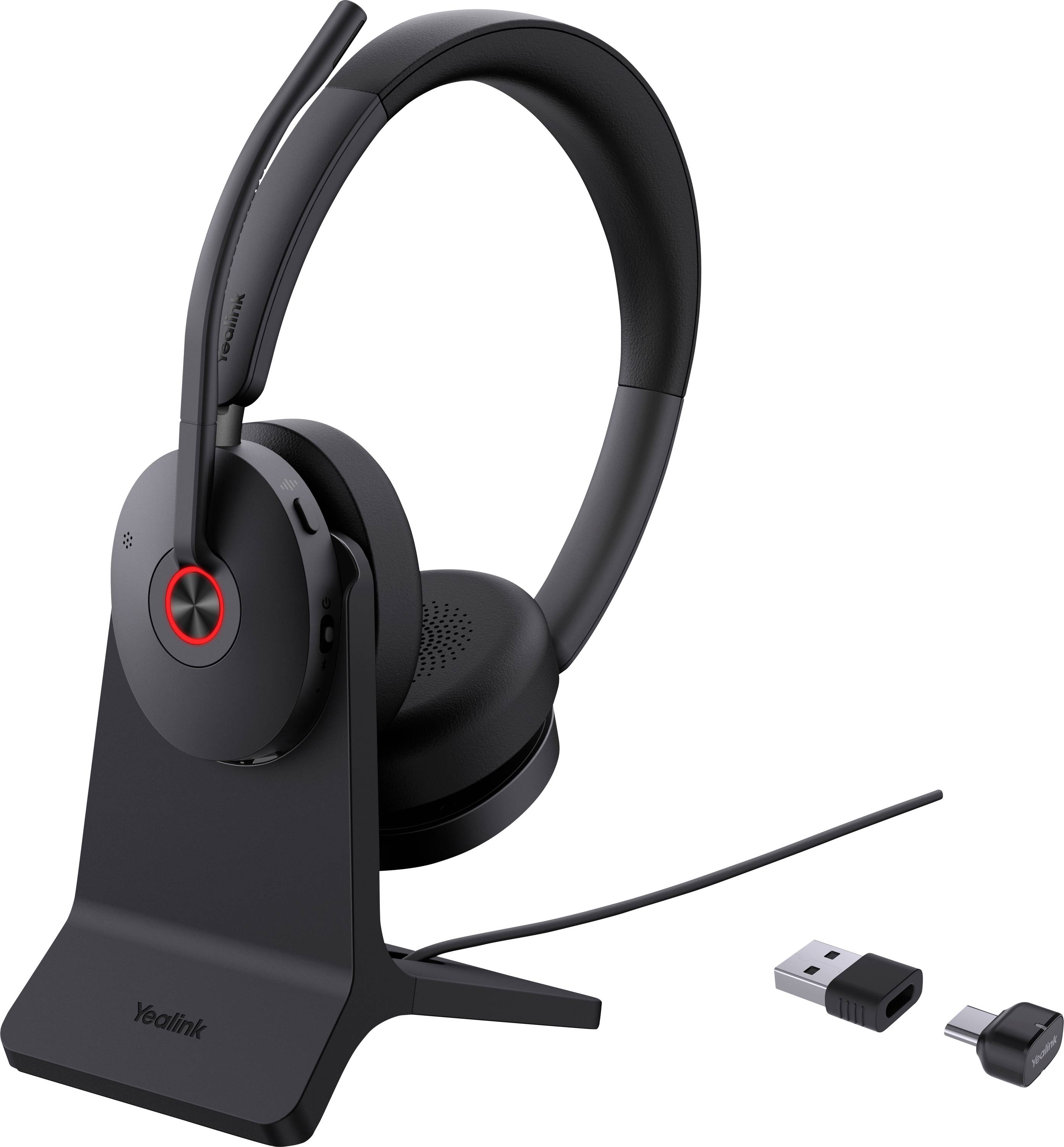 Un casque audio sans fil de couleur noire avec microphone intégré sur un socle de charge, accompagné d'un adaptateur USB et d'un connecteur, adapté à l'utilisation informatique.