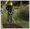 Une personne portant un équipement de protection taille l'herbe avec un outil électrique près d'un parterre de jardin entouré de paillis d'écorce dans une cour paysagée.