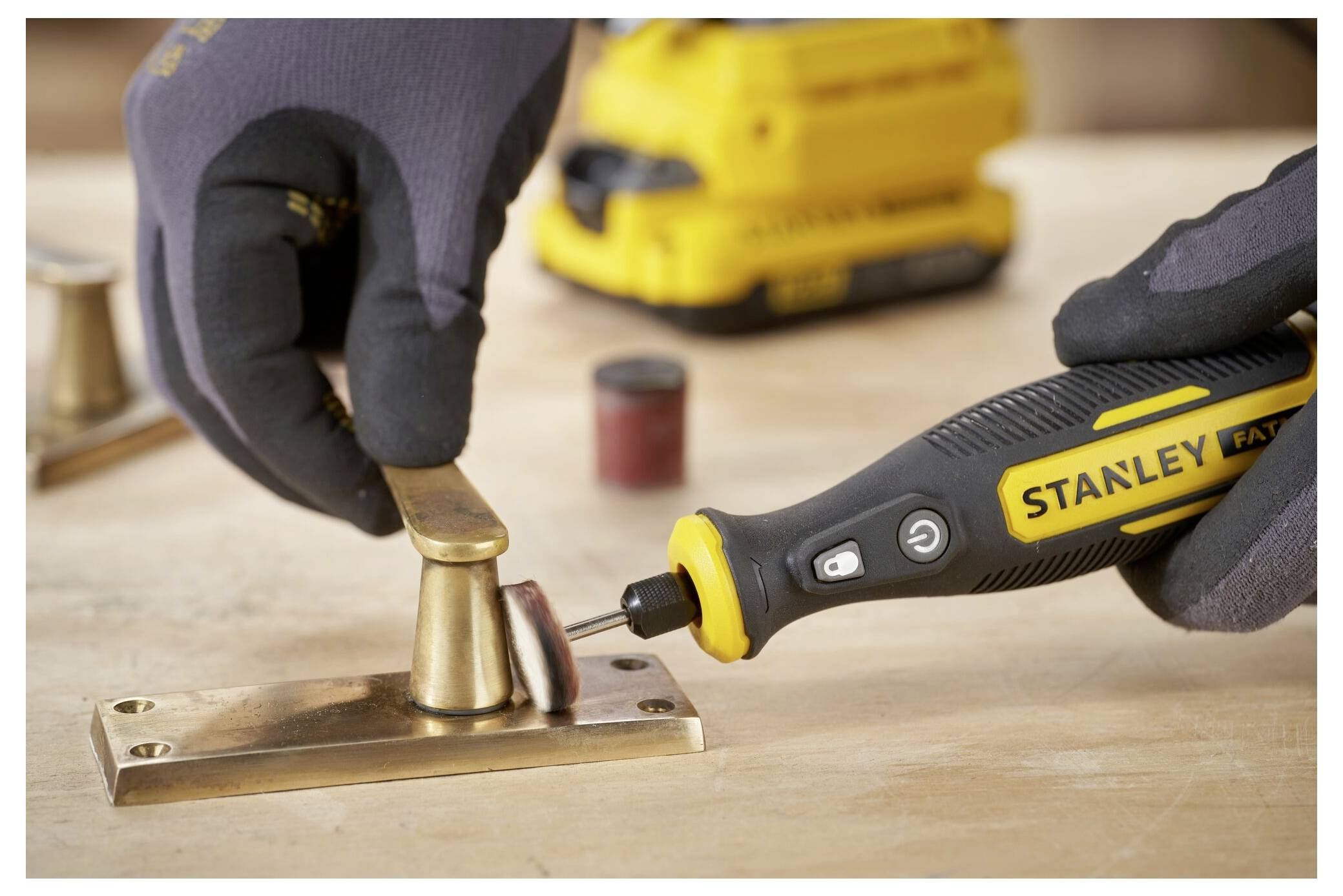 Outil rotatif de marque « Stanley » utilisé pour polir une poignée de porte en laiton sur une surface en bois, en mettant l'accent sur un travail de finition détaillé.