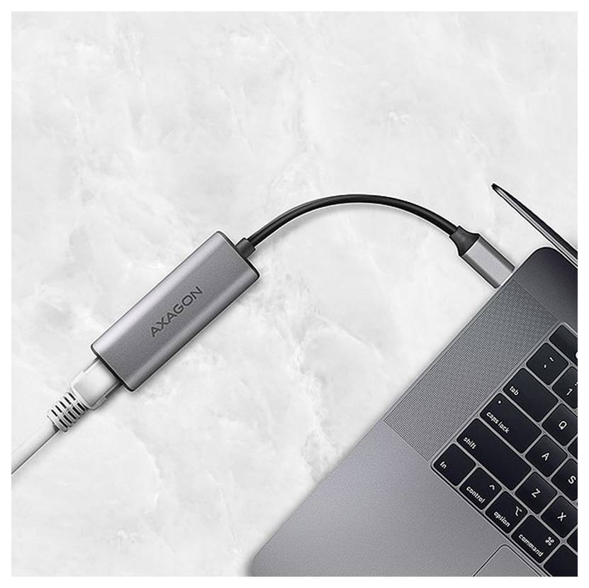 Un ordinateur portable connecté à un câble blanc via un adaptateur AXAGON gris sur une surface en marbre.