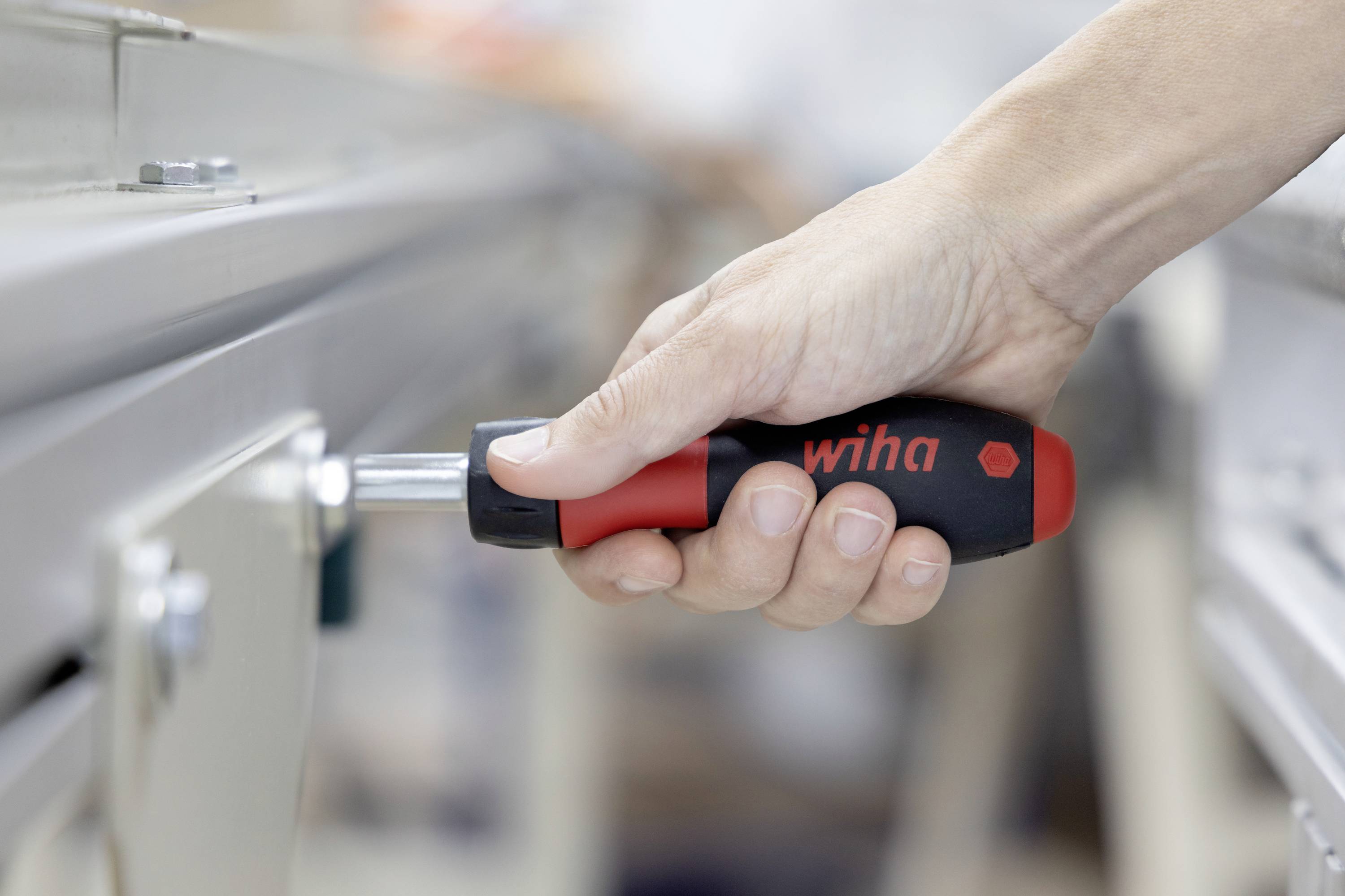 Gros plan d'une main utilisant un tournevis Wiha pour ajuster un panneau de machine métallique ou une fixation.