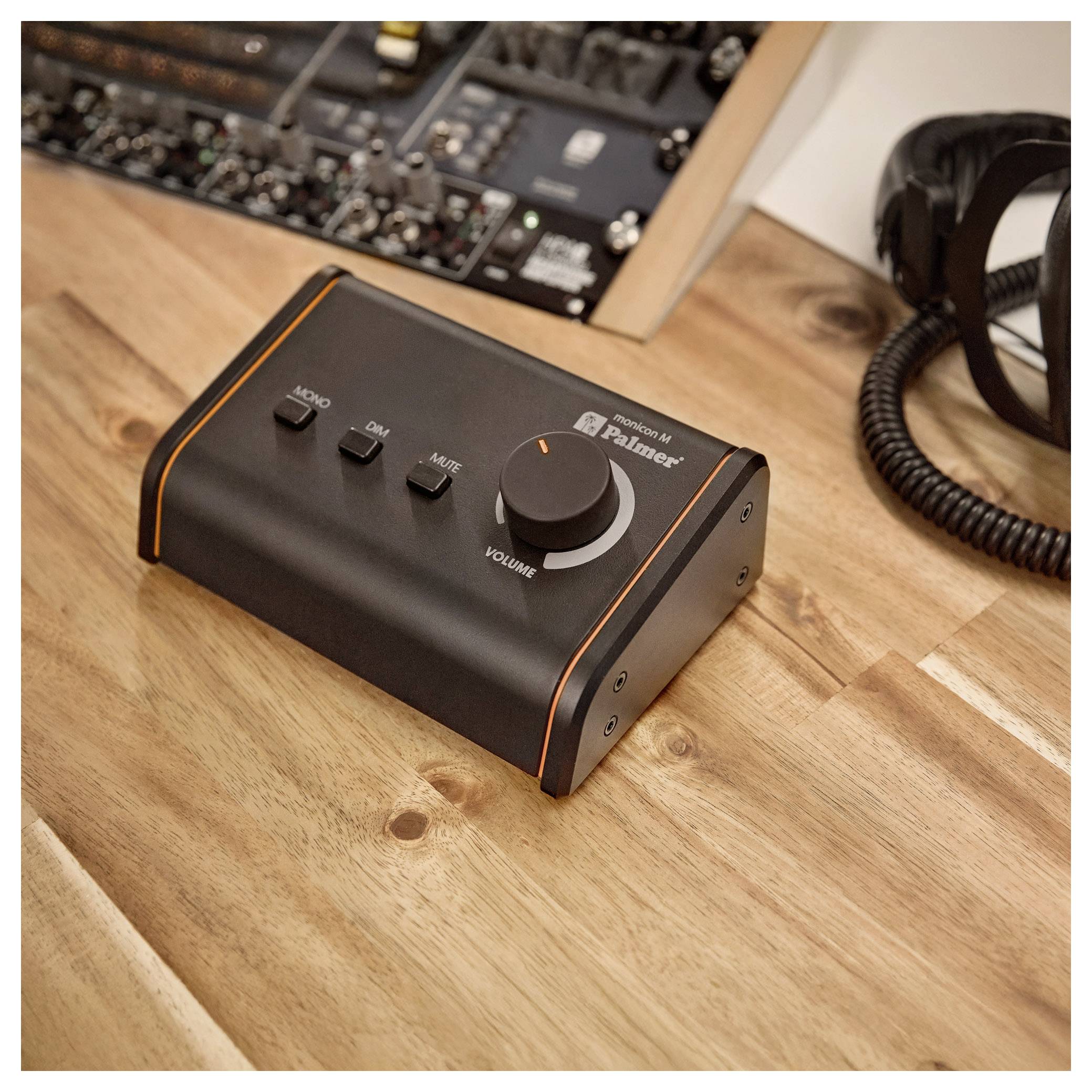 Boîte de contrôle audio de bureau noire sur une table en bois, avec un bouton de volume et des boutons mono, d'atténuation et de sourdine.
