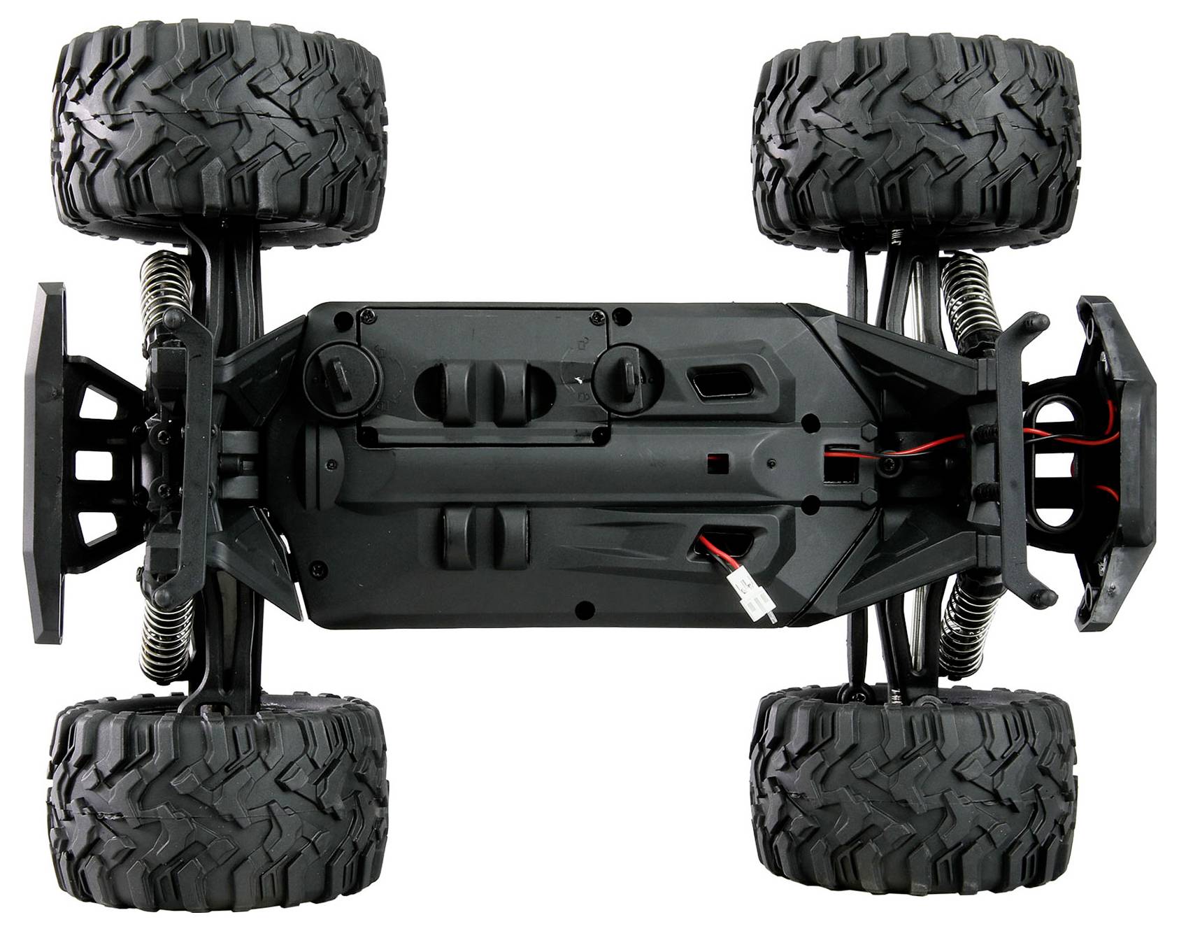 Vue de dessous d'un châssis de camion RC tout-terrain à quatre roues avec suspension, gros pneus crantés et câblage apparent.