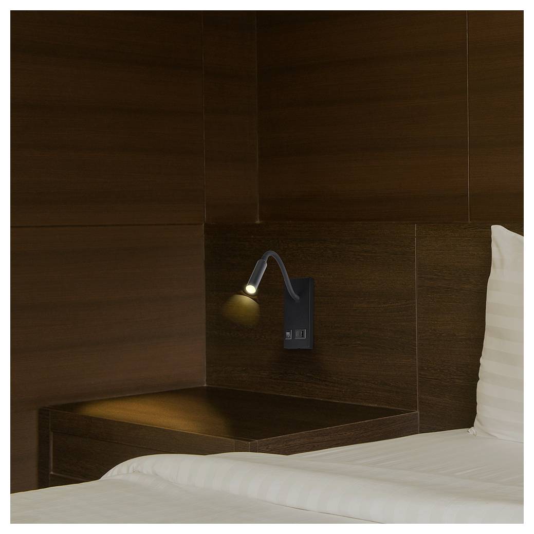Petit coin de chambre d'hôtel minimaliste avec une lampe de lecture fixée au mur au-dessus d'une tablette de nuit, à côté d'un lit blanc et d'un oreiller.