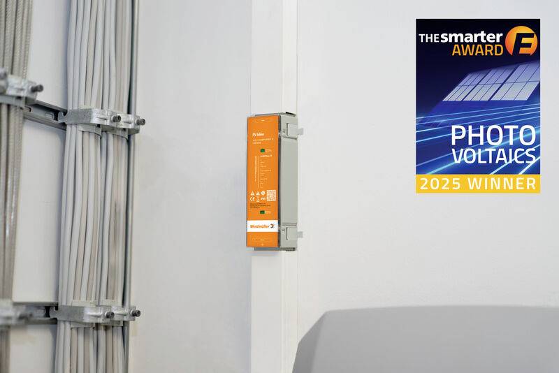 Composant électrique orange fixé au mur à côté de conduits de câbles, avec un autocollant « The smarter E AWARD » « PHOTO VOLTAICS 2025 WINNER » sur le mur.
