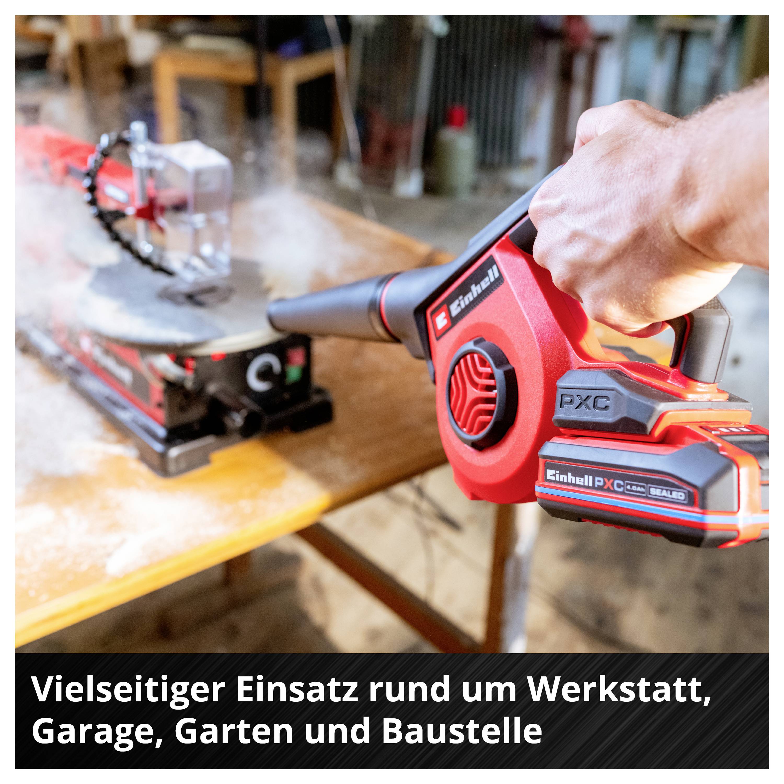 Souffleur de feuilles à batterie rouge tenu à la main soufflant des feuilles sur un établi; Texte: « Utilisation polyvalente autour de l'atelier, du garage, du jardin et du chantier »