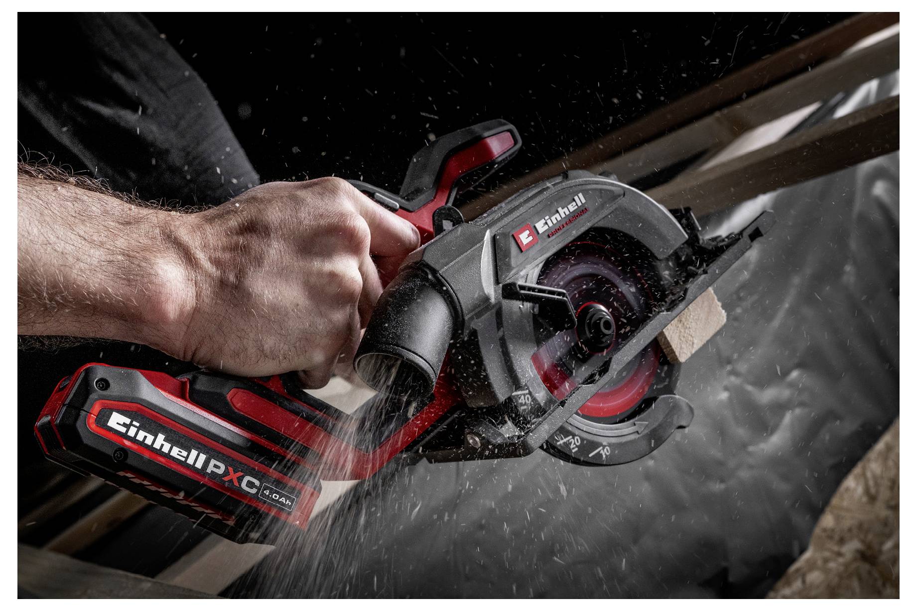 Gros plan d'une personne utilisant une scie circulaire sans fil Einhell rouge et noire pour couper du bois, avec de la sciure qui vole.
