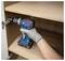 Main gantée utilisant une perceuse sans fil Bosch pour serrer une charnière d'armoire à l'intérieur d'une unité d'étagère en bois.