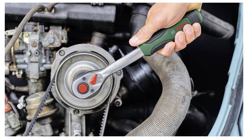 Gros plan d'une personne utilisant une clé à cliquet pour serrer une poulie de courroie moteur dans le compartiment moteur d'une voiture.