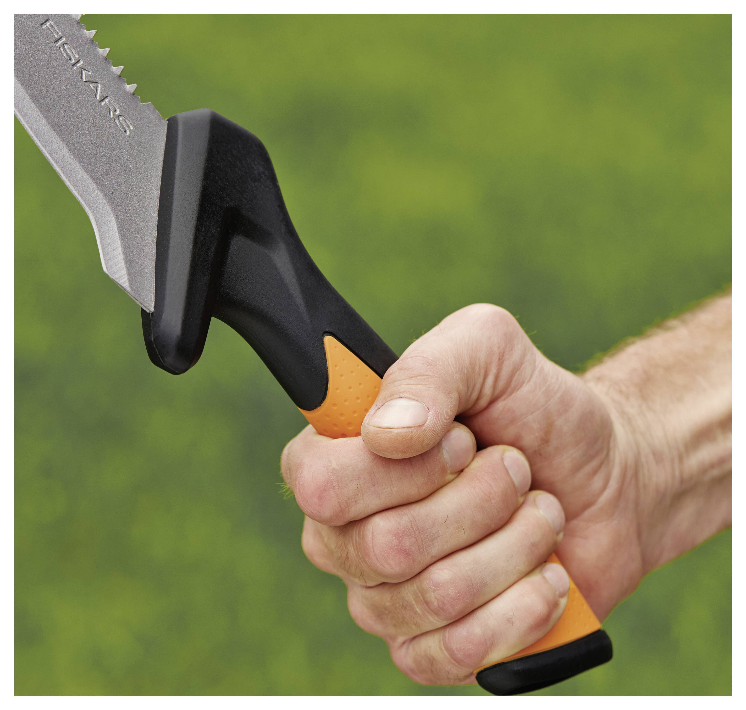 Gros plan d'une main saisissant le manche noir et orange d'un couteau Fiskars sur un fond vert flou.