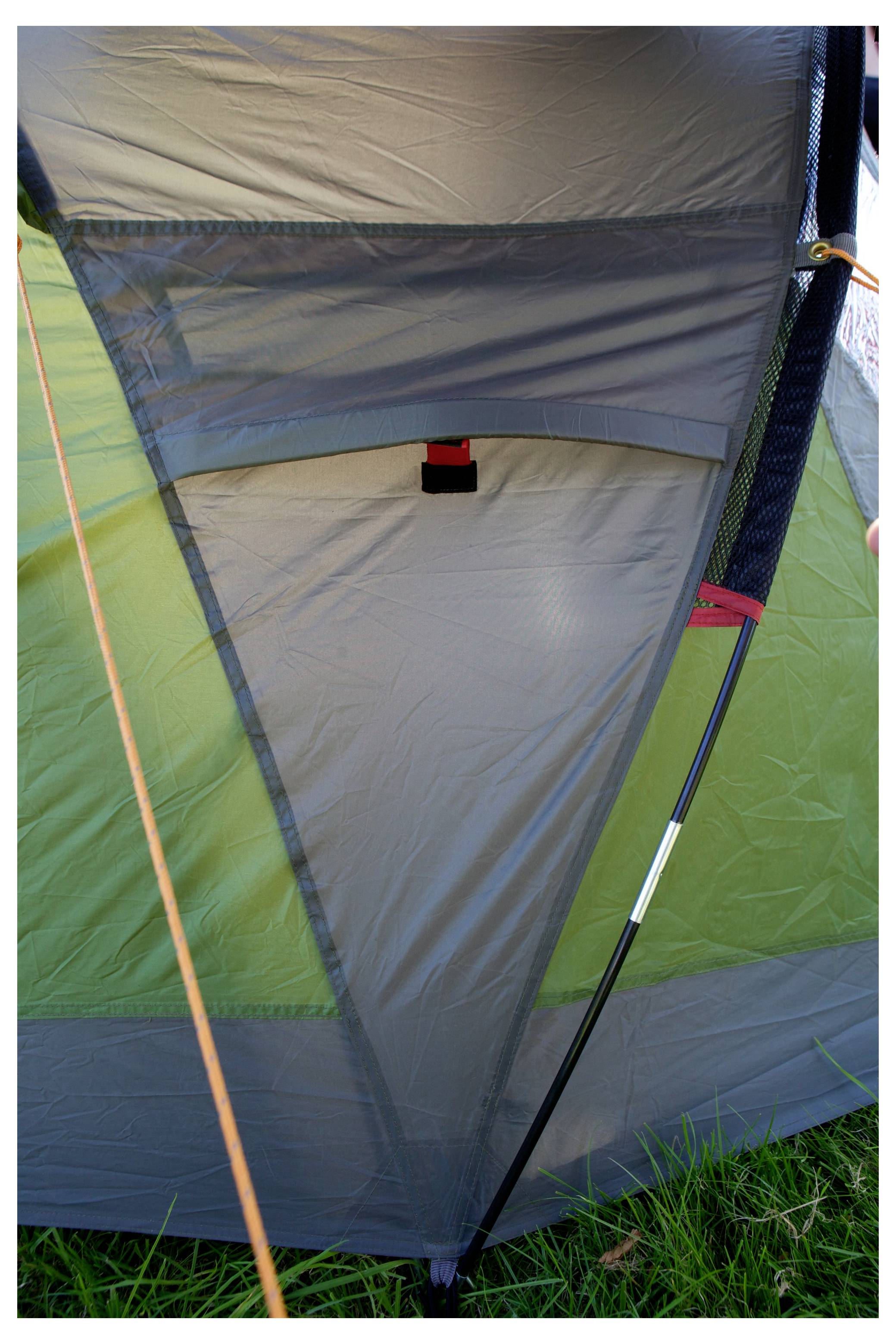 Gros plan de la paroi intérieure d'une tente et de l'entrée avec des poteaux et de l'herbe visibles à l'extérieur, montrant la structure en tissu et l'ouverture.