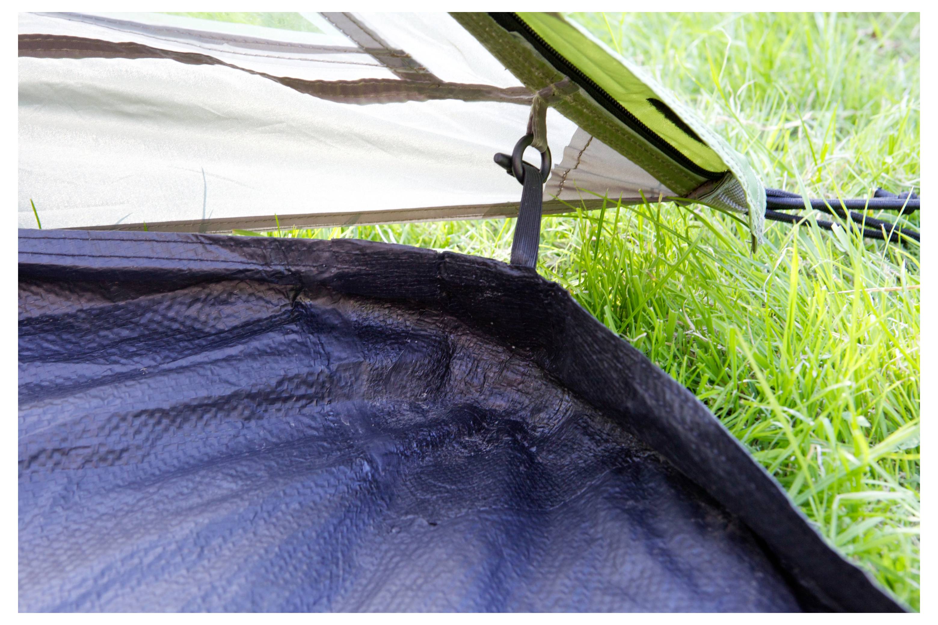 Gros plan d'une toile de tente et d'un tapis de sol reliés par une sangle et une pince, montrant l'installation de l'abri sur l'herbe.
