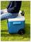 Personne assise sur une glacière bleue avec roues sur l'herbe à l'extérieur, l'utilisant comme siège et chariot portable.