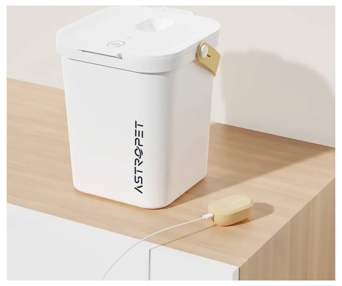 Bac à déchets pour animaux de compagnie blanc ASTROPET avec couvercle et poignée latérale sur une surface en bois, présenté avec un petit appareil beige connecté à l'avant.