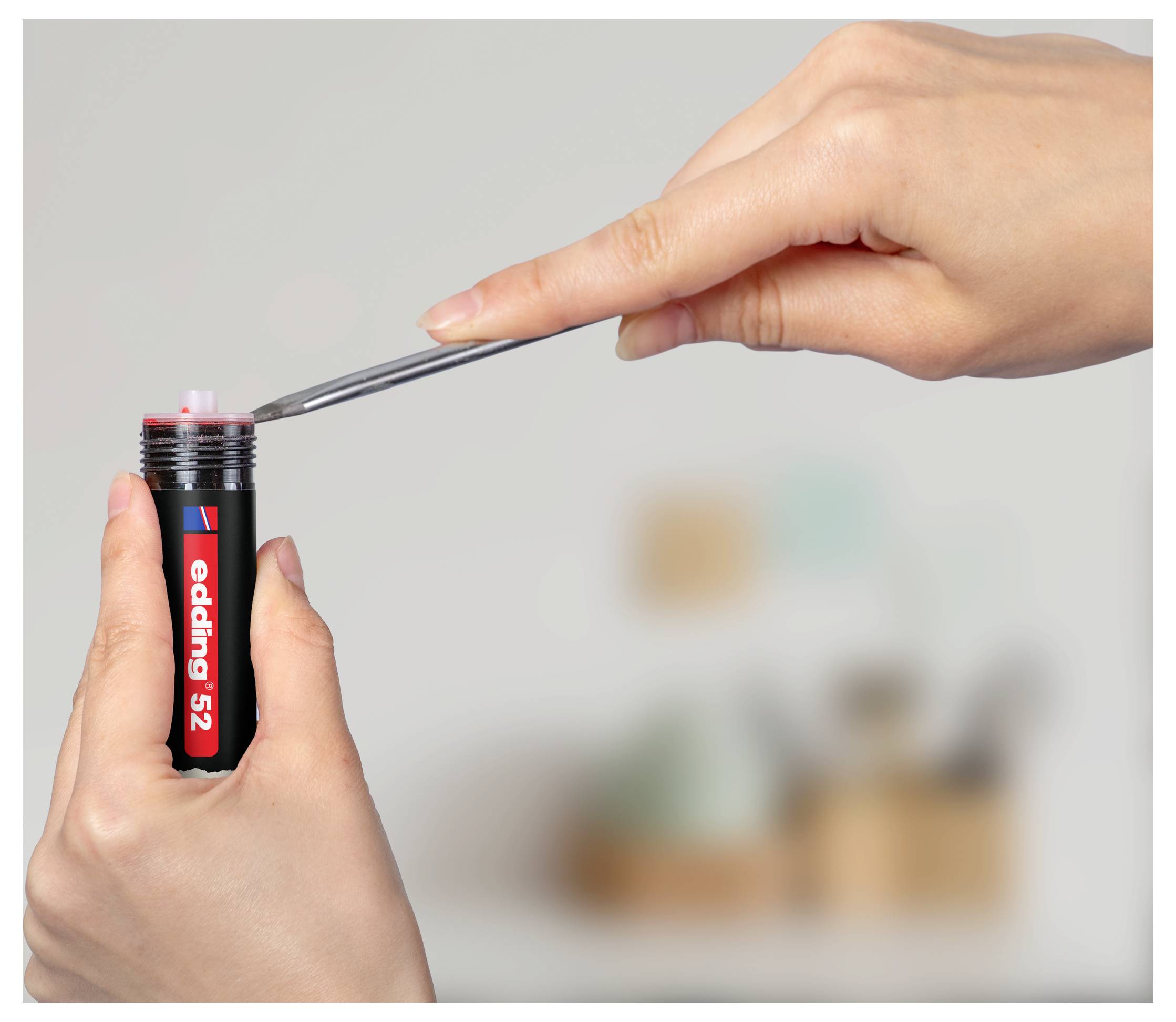 Des mains utilisant des pincettes pour retirer la pointe d'un marqueur rouge « edding 52 » d'un tube noir