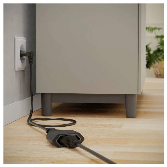Cordon d'alimentation noir branché dans une prise murale à côté d'une armoire, avec le cordon qui s'enroule sur un plancher en bois.